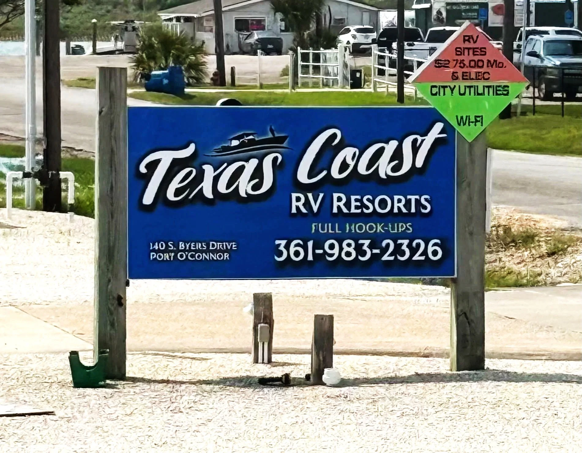 Sign for Texas Coast RV Resorts, located at 140 S Byles Drive, Port O'Connor. Contact phone number is 361-983-2326. The sign is blue with white text and has an illustration of a boat on the water. There is a smaller, multicolored sign above it with information about RV site sizes, city utilities, and Wi-Fi.