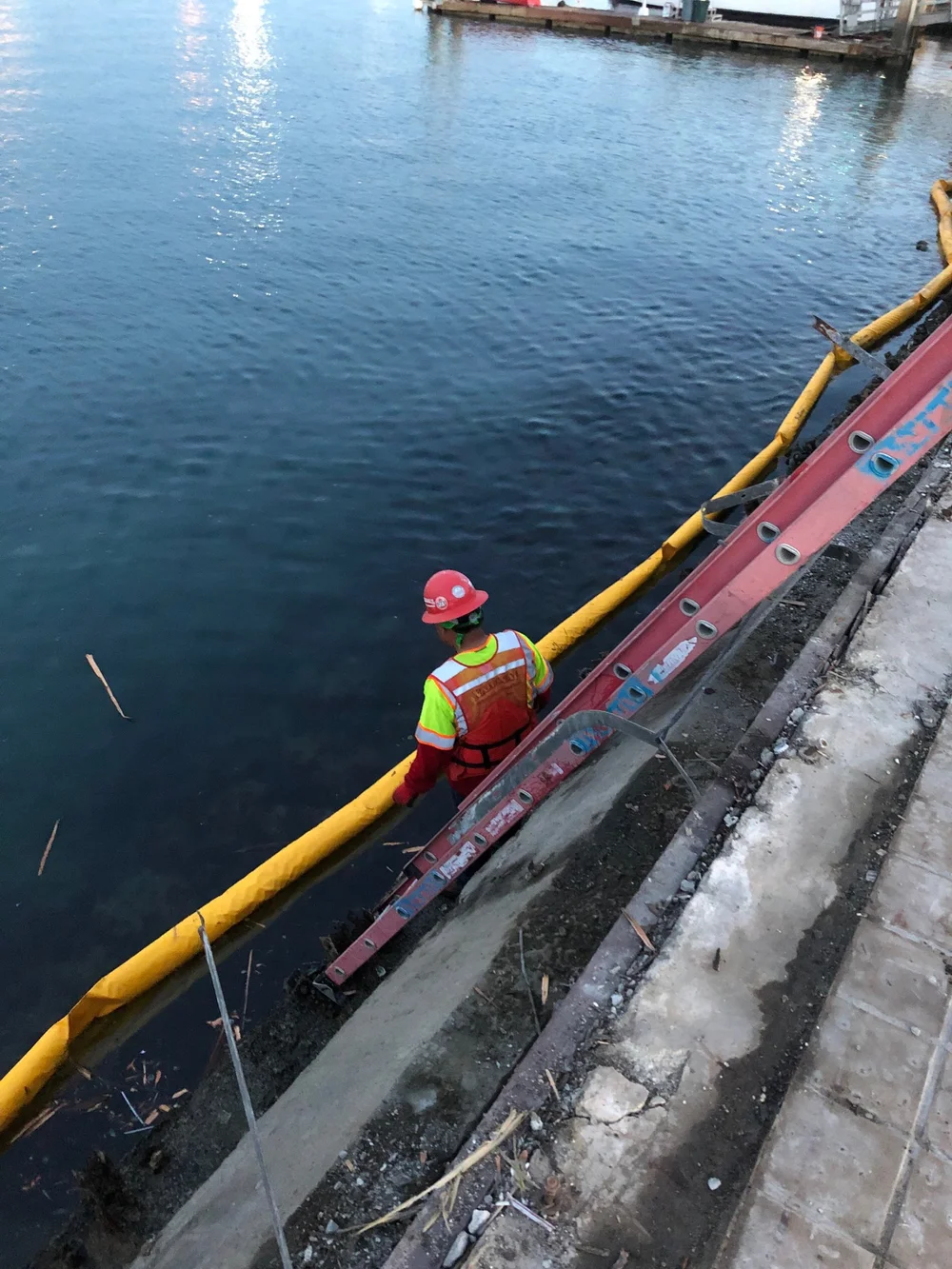 Worker beside a containment barrier along a waterfront