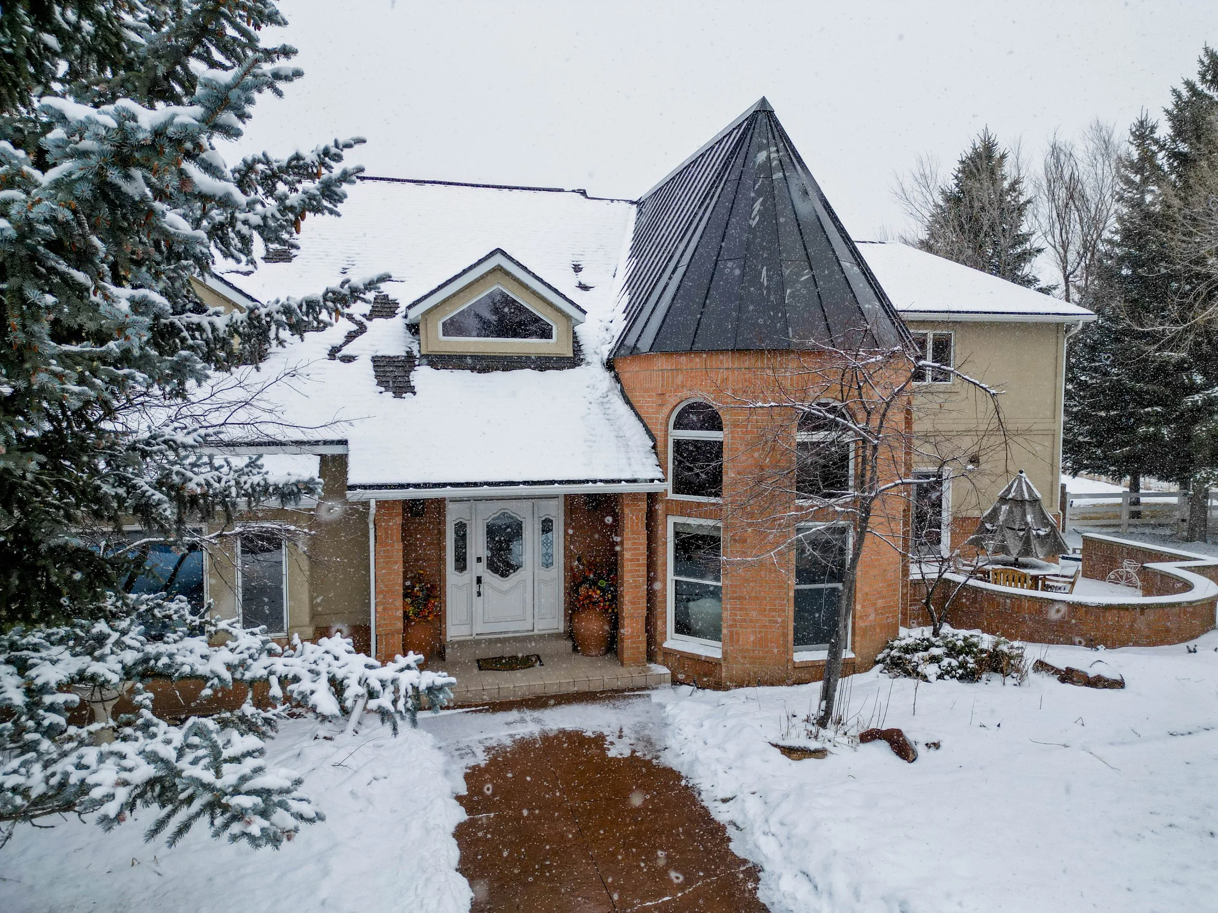 Foxtail rental home with a snow-covered roof and a mix of brick and beige siding, surrounded by snow and trees, with a driveway leading to the front door.