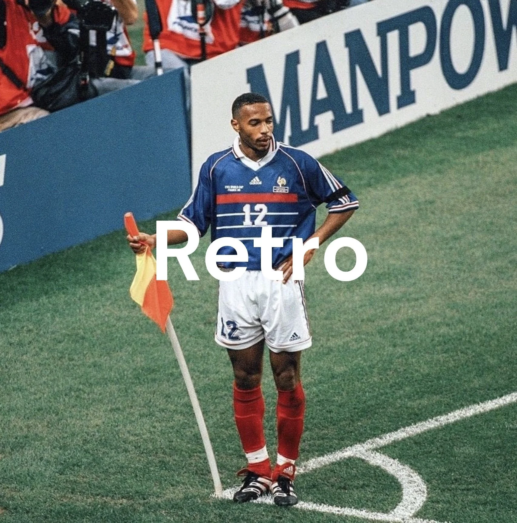 A soccer player standing by the corner flag on the field, wearing a blue and white jersey with the number 12, red socks, and black soccer shoes, with his hand on his waist and holding the corner flag, during a game or practice.