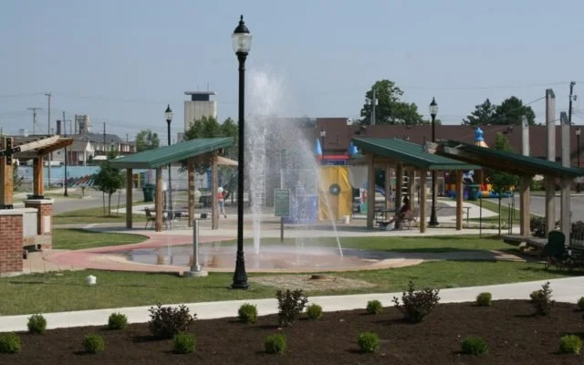 Public park with water fountain, covered picnic areas, playground equipment, and walking paths.