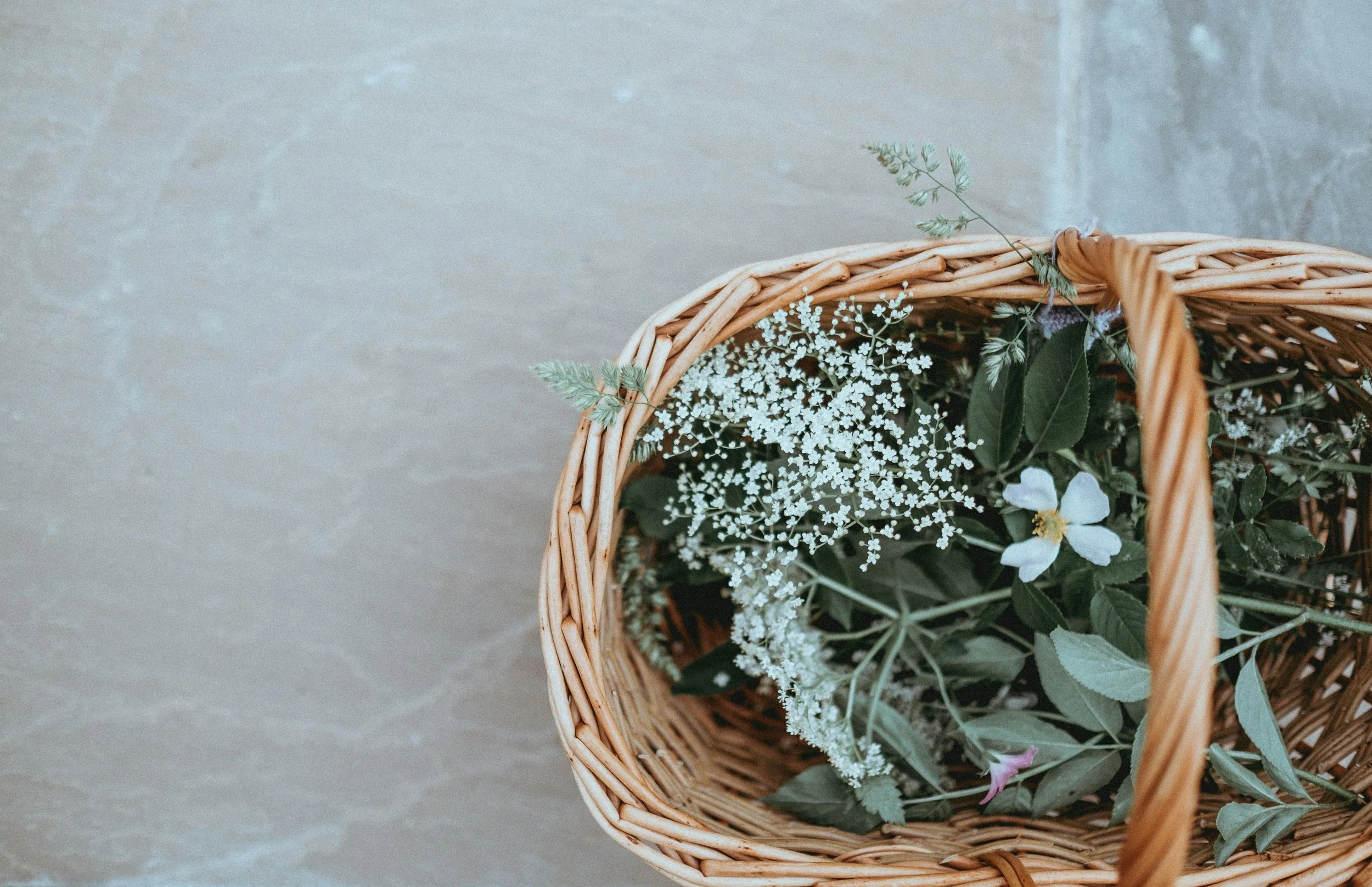 A wicker basket filled with white and green flowers on a gray surface.