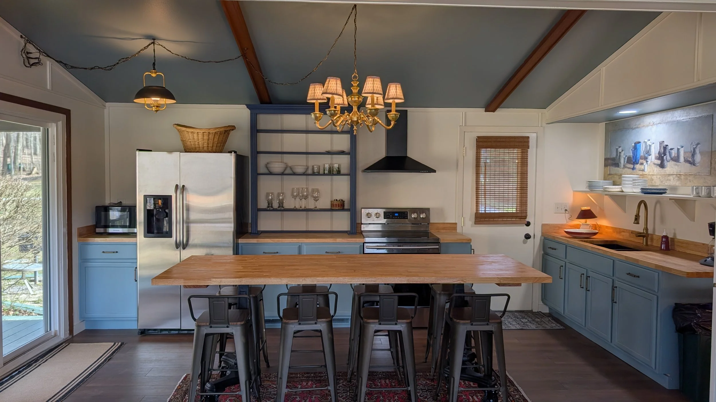 Bright, open plan kitchen with blue cabinetry, stainless steel appliances and large dining and prep table. 