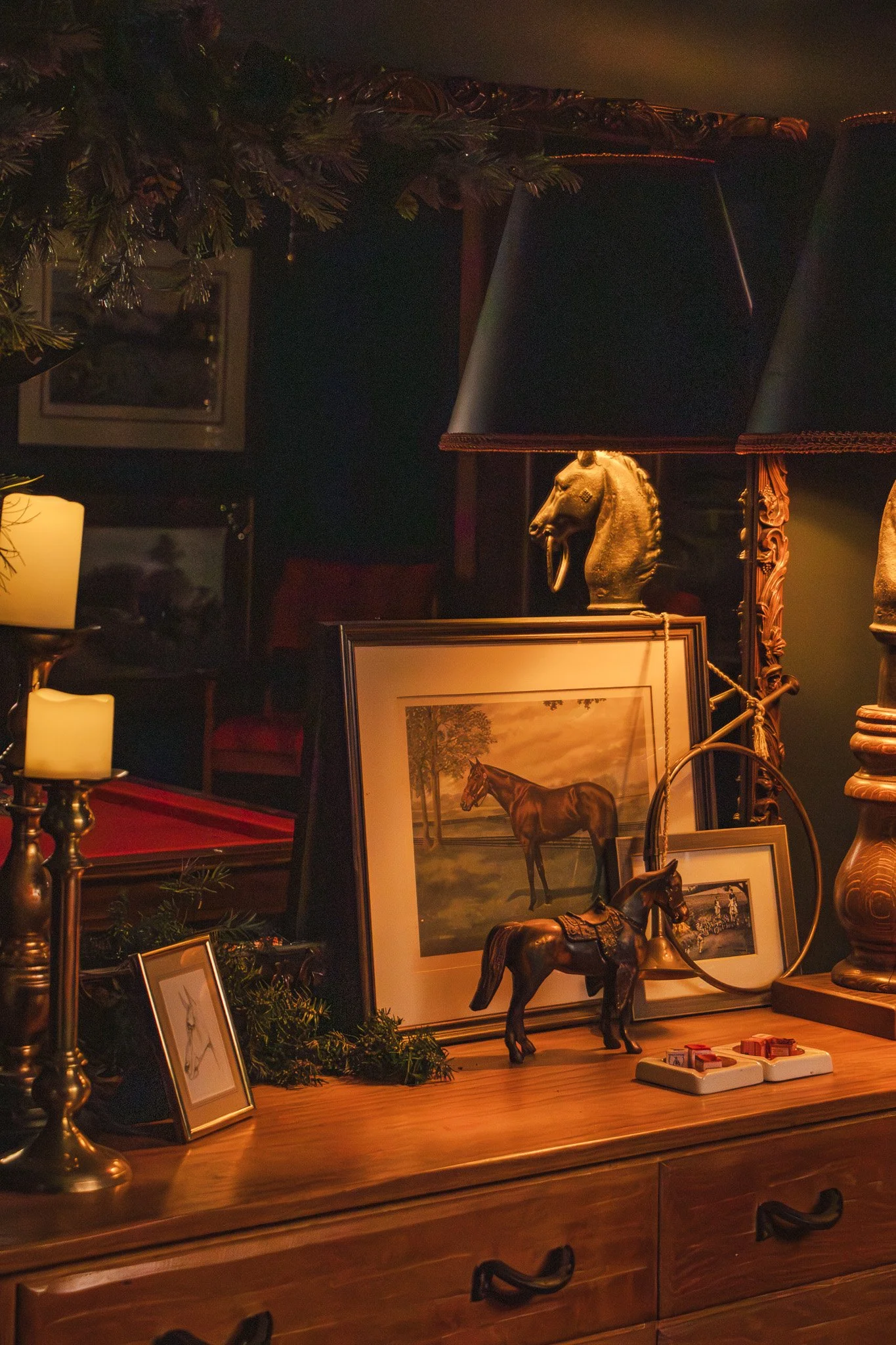 Decorative table with framed horse artwork, horse figurines, lamps, and candles in a cozy, dimly lit room.