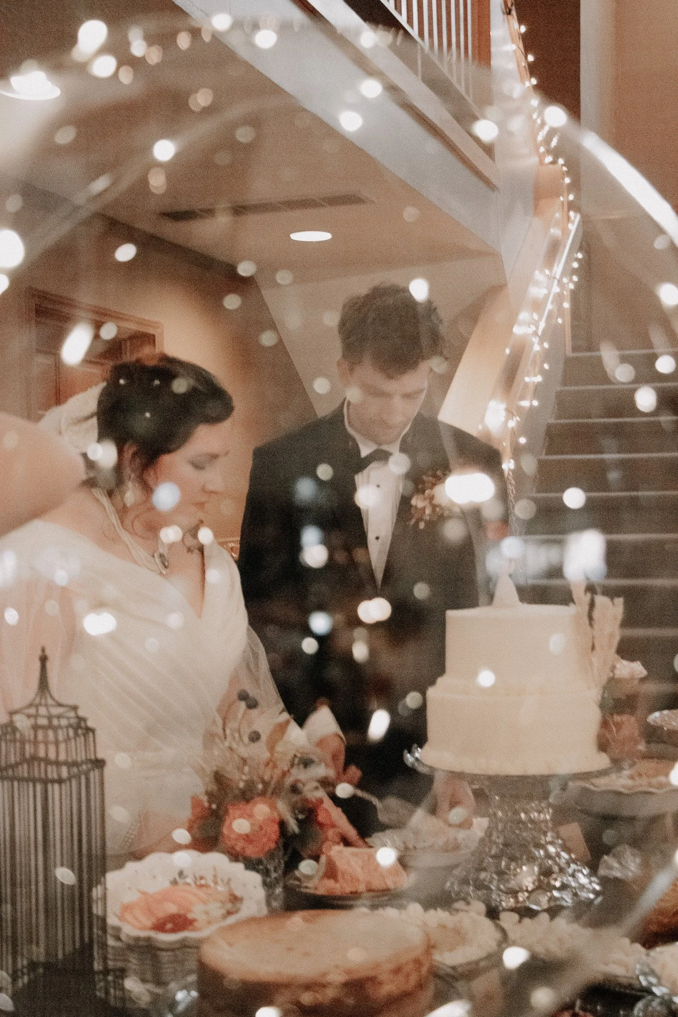 Reflection of a bride and groom at the wedding cake table, with the bride dressed in a white dress and the groom in a tuxedo, surrounded by wedding decorations and food.