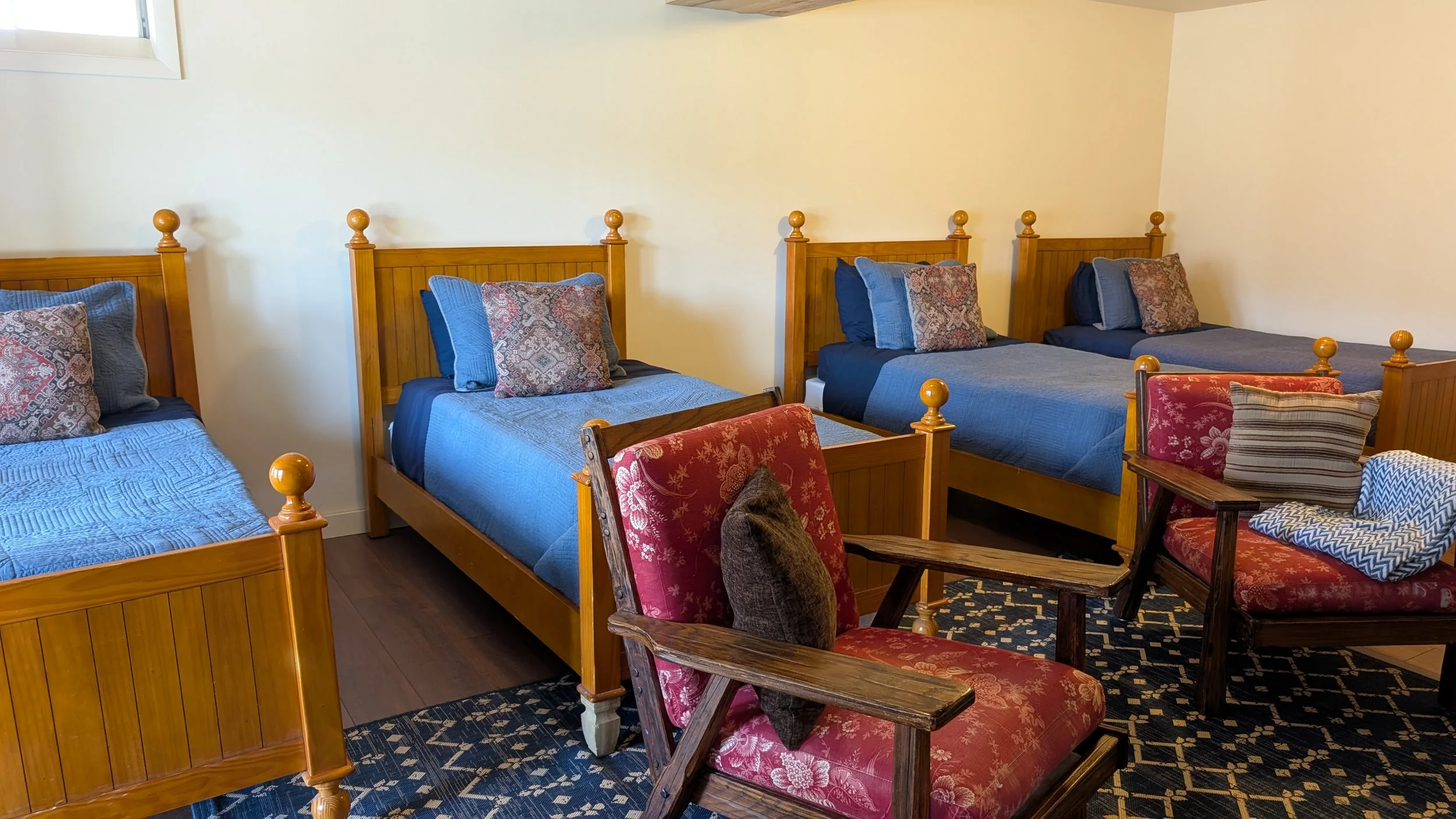 A cozy bedroom with four wooden, twin-size beds with navy bedding, and a glass sliding door with beige curtains leading outside.