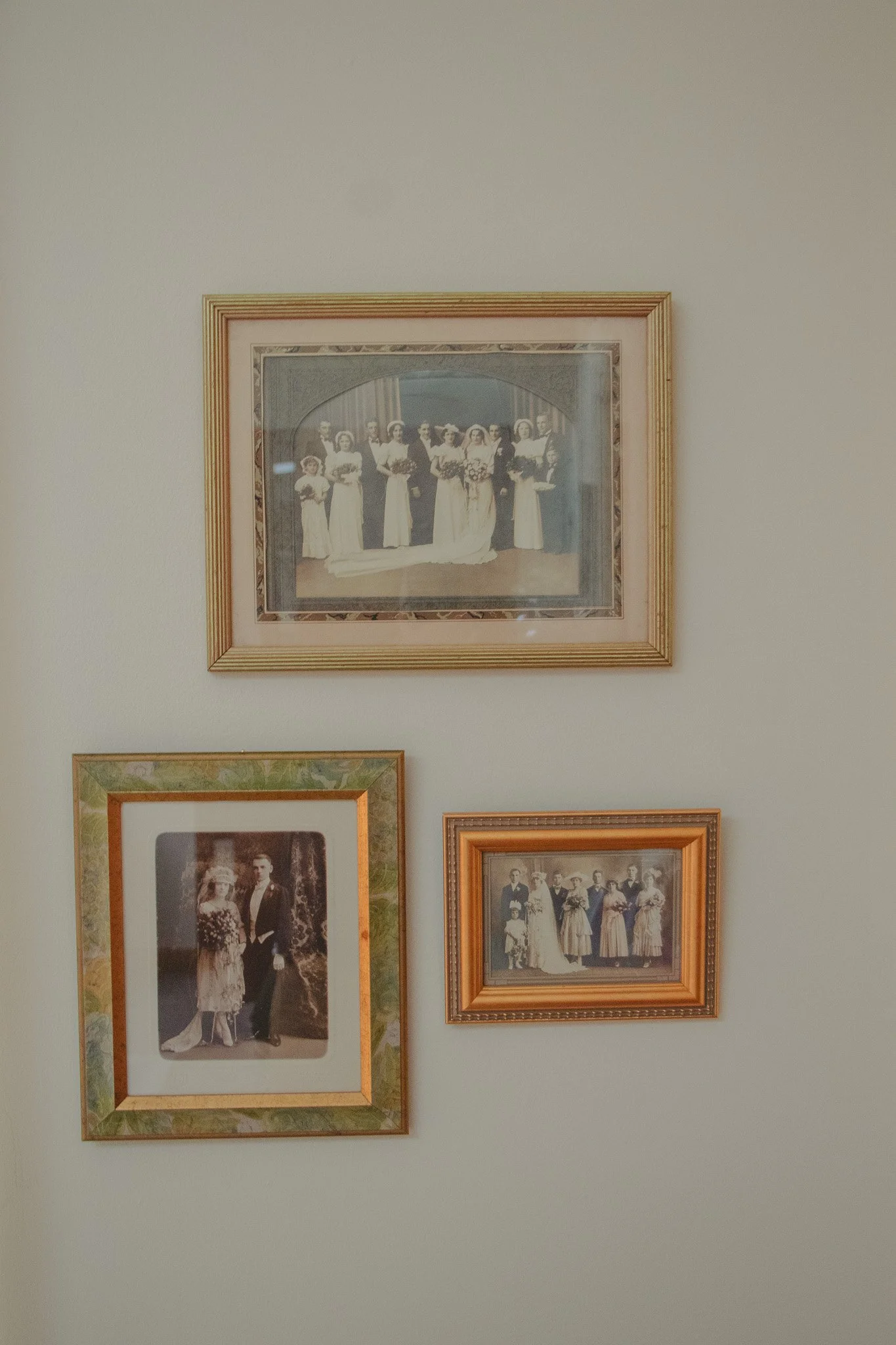 A wall with three framed vintage black-and-white photographs of people, arranged with one larger photo above two smaller ones.