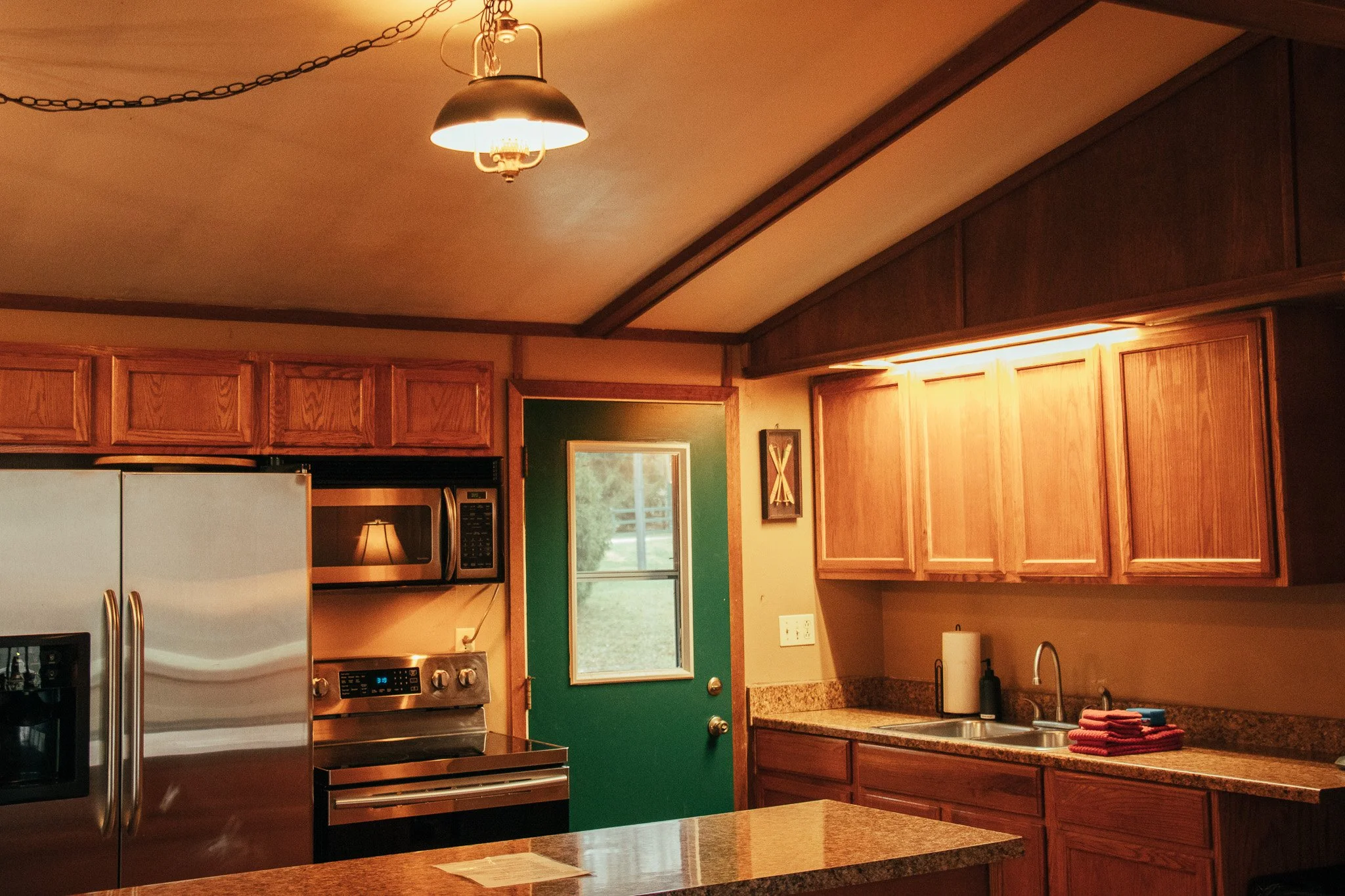 Kitchen with wooden cabinets, granite countertops, stainless steel appliances, a green door, and a window showing outdoor greenery.