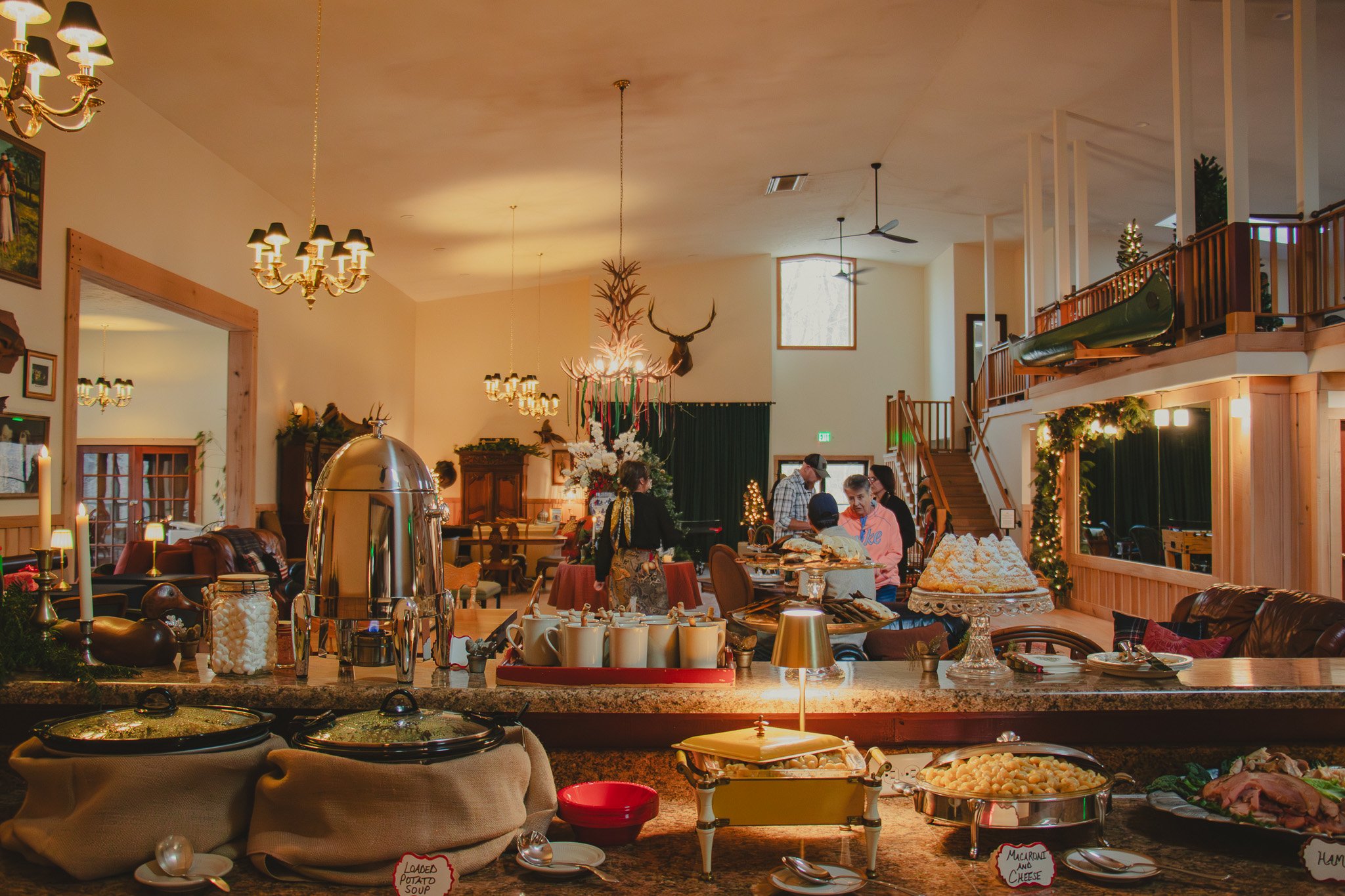 A buffet setup in a warmly lit dining area with Christmas decorations, including a large cake, crockpot dishes, and people serving food.