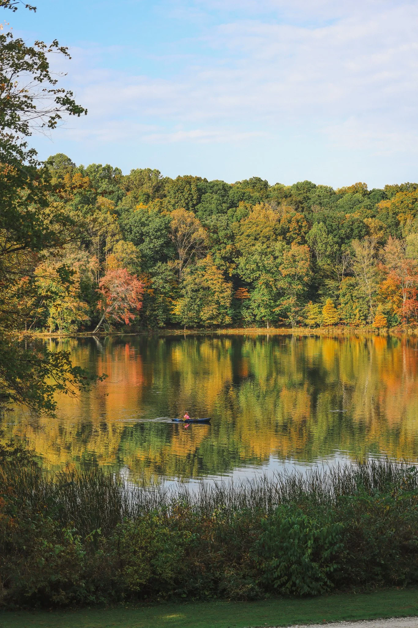 A lake with fall-colored trees surrounding it, reflecting on the water, with a person kayaking.
