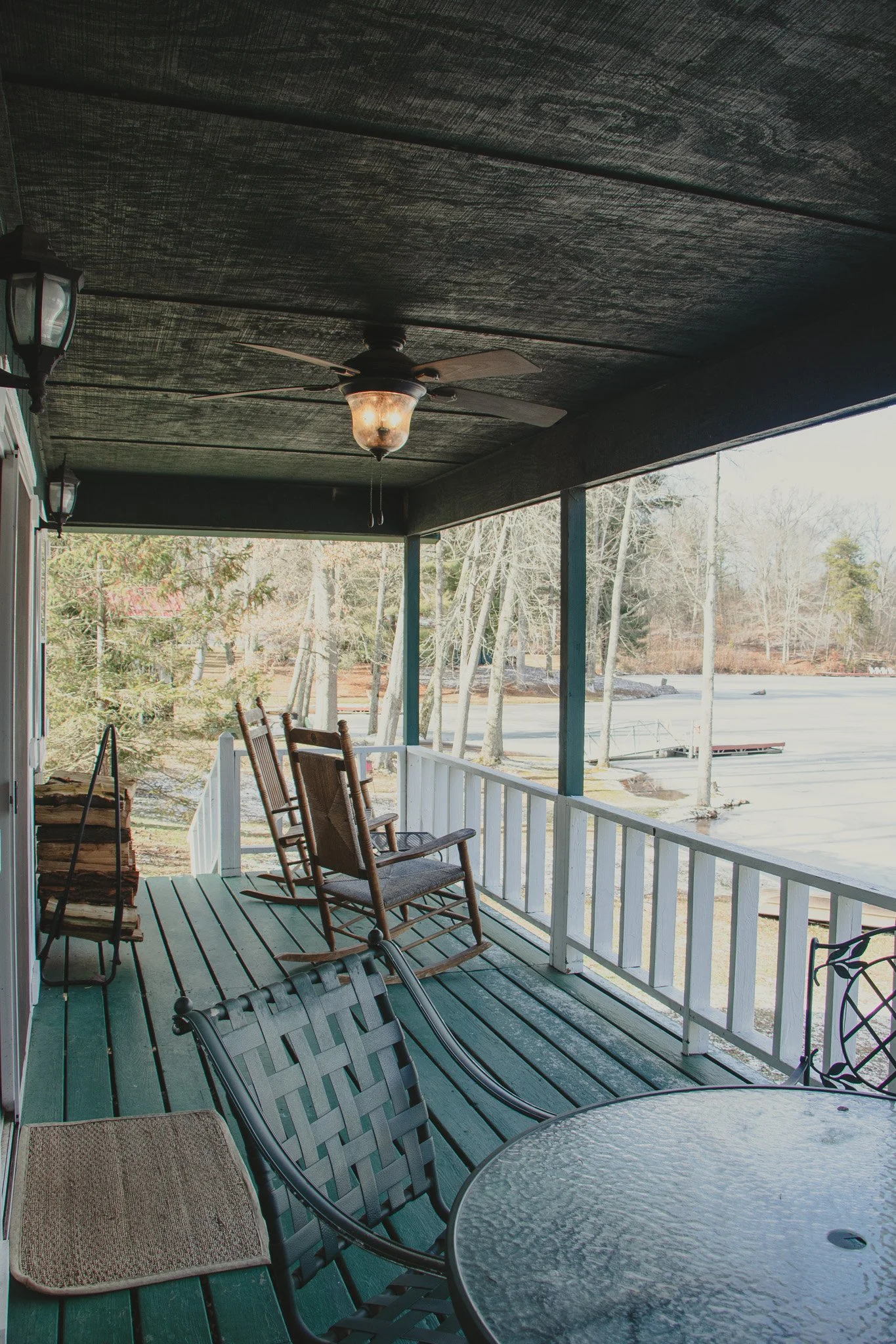 Covered porch with patio furniture overlooking a frozen pond and leafless trees in winter.