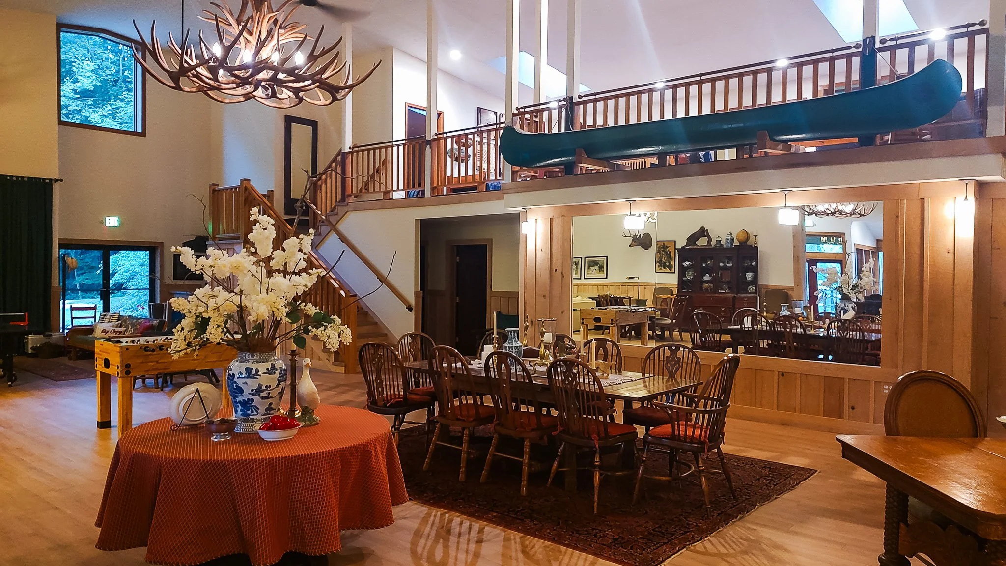 Interior of a spacious house with a dining area, a staircase, a sunny window, and a loft with a slide, decorated with wooden furniture and floral decor.