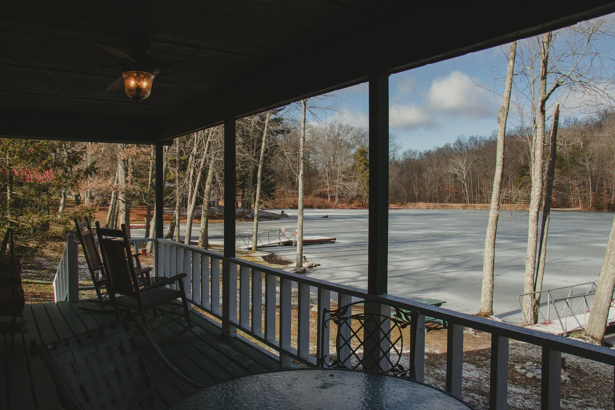 Porch with chairs overlooking a frozen lake with leafless trees and a cloudy sky in winter
