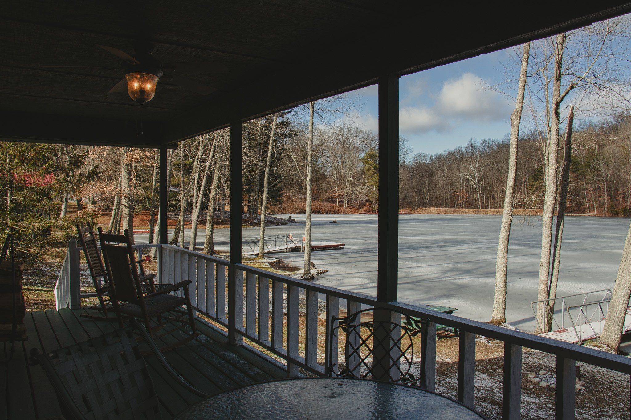 Porch with chairs overlooking a frozen lake with leafless trees and a cloudy sky in winter