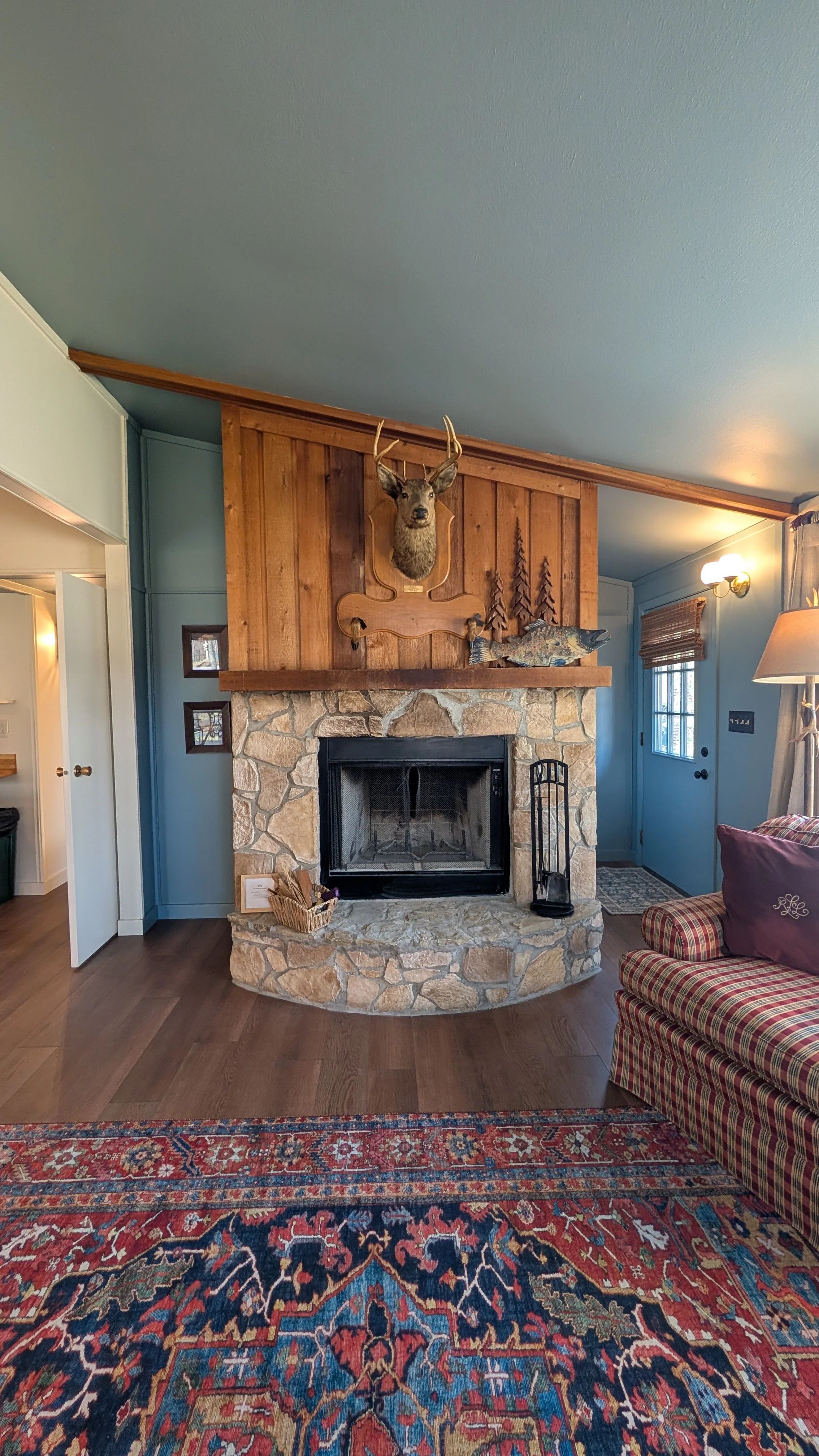 Interior room of cabin with wood burning fireplace, open-concept living room and kitchen overlooking the lake.