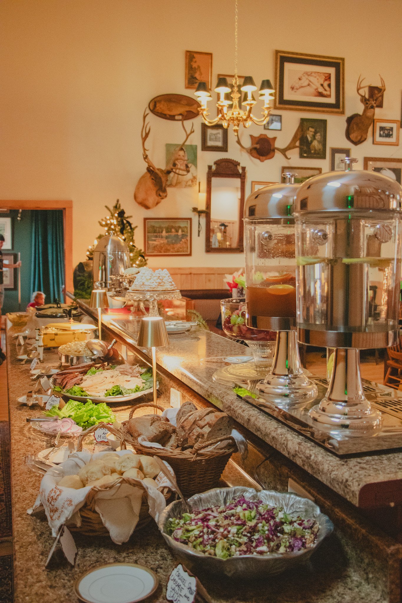A buffet with various dishes such as bread, salad, and cold cuts in a rustic restaurant decorated with mounted deer heads and framed artwork.