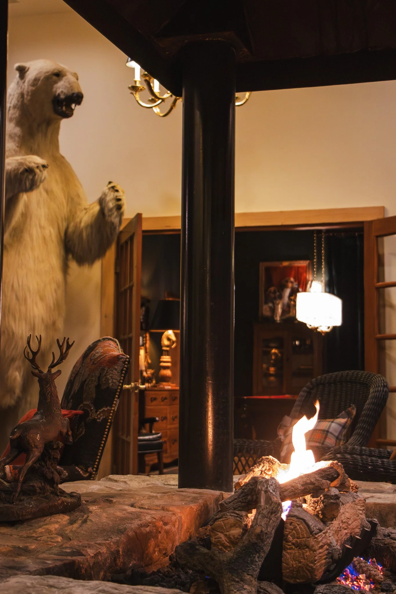 A cozy room with a fireplace, a mounted bear on the wall, a small deer sculpture on a table, and various vintage furniture and lighting.