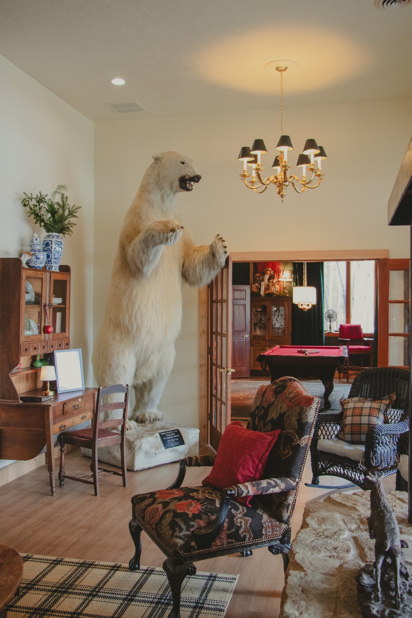 A taxidermy polar bear standing on a platform in a living room, surrounded by vintage furniture and decor.