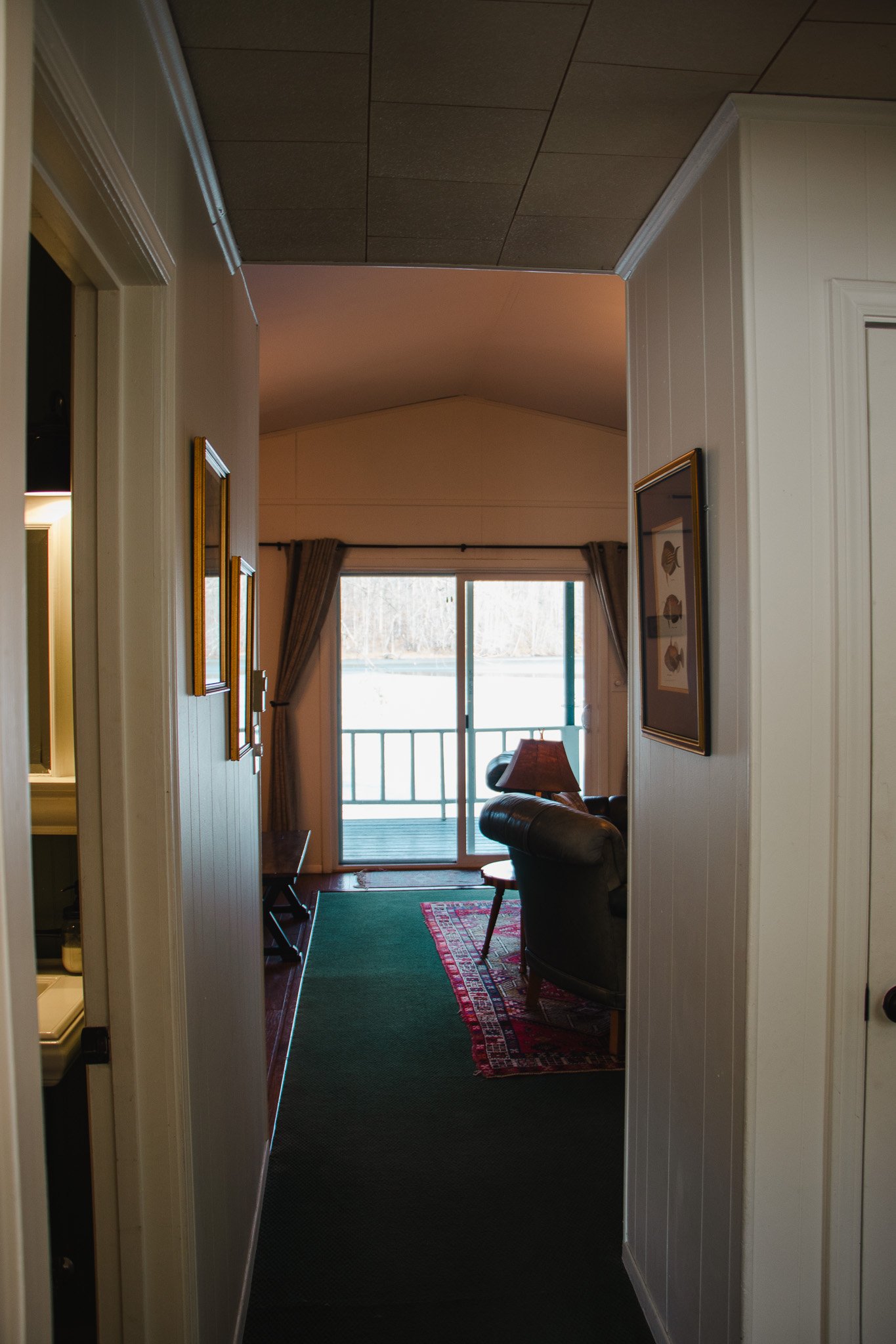 Interior view of a living room with a sliding glass door leading to a balcony, featuring two leather chairs, a lamp, a patterned rug, and curtains.