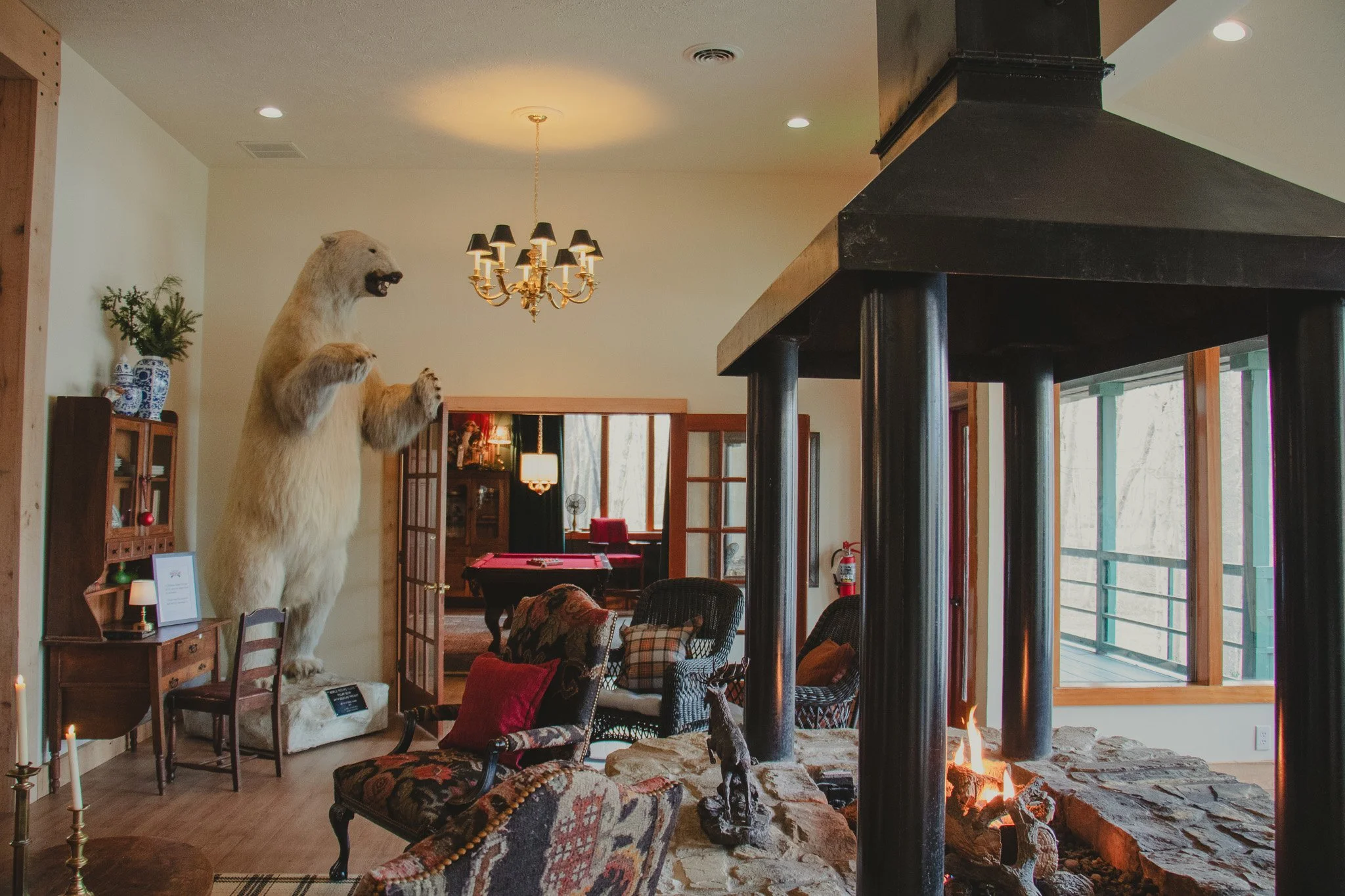 Interior living room with a mounted polar bear, fireplace, armchairs, and a pool table in the background.
