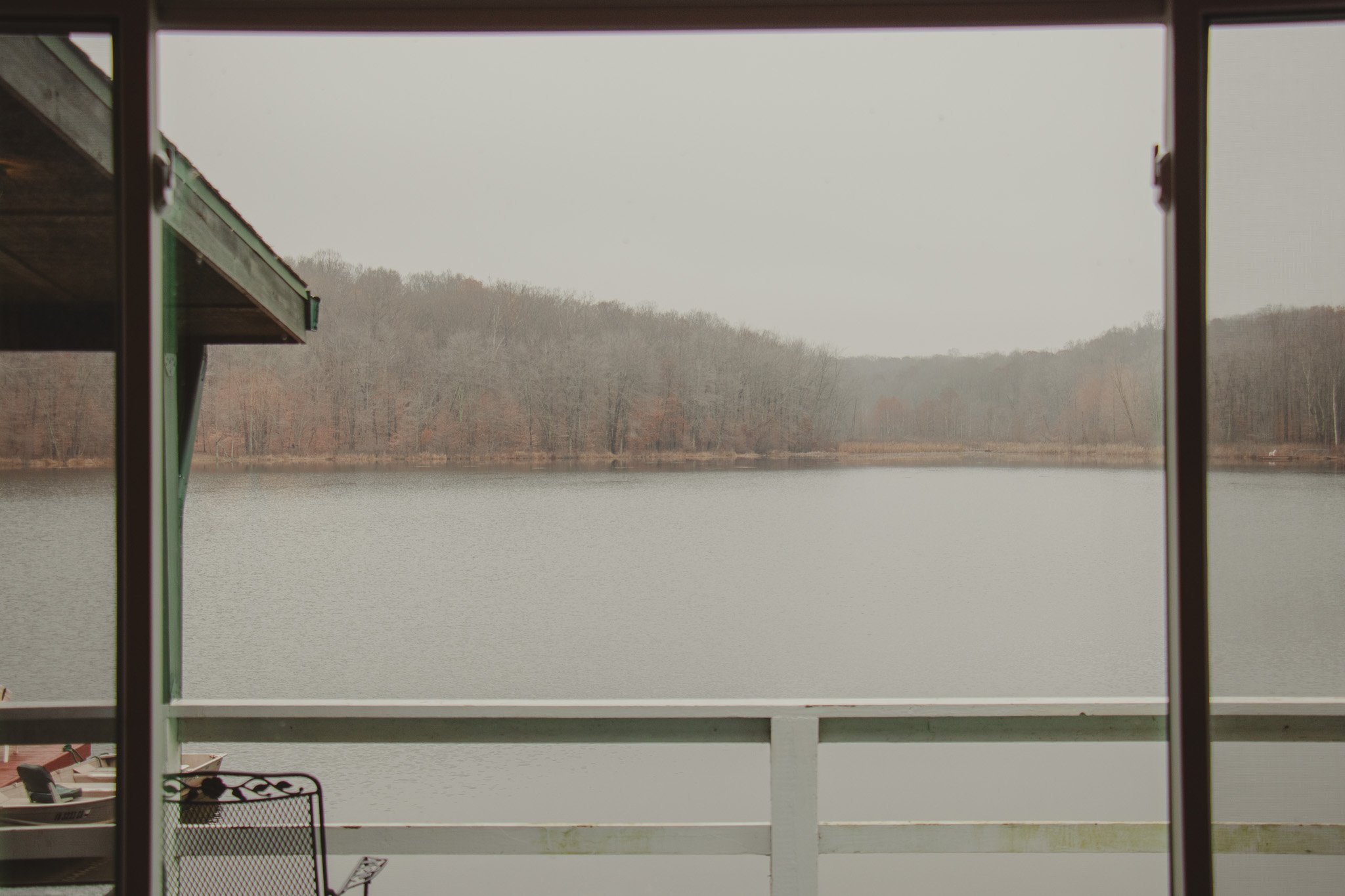 View of a lake surrounded by leafless trees, seen from a balcony with open sliding glass doors.