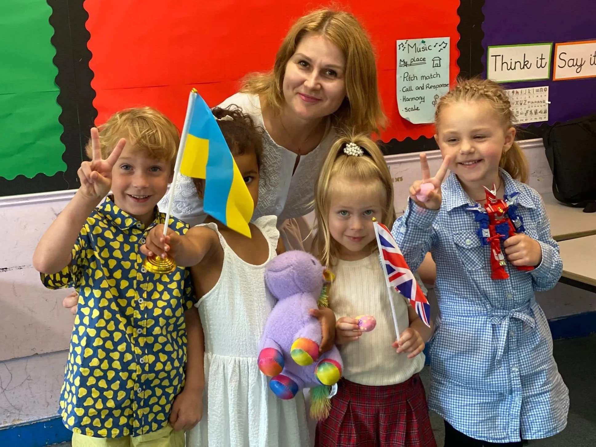 Group of children and an adult in a classroom decorated with outdoor and holiday-themed decorations, celebrating joyfully.