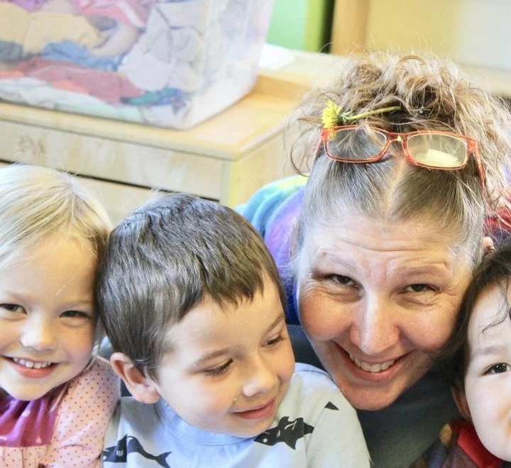 A woman with glasses on her head smiling with three children.