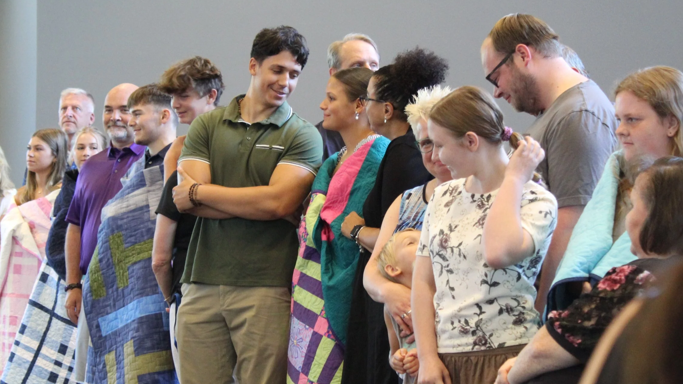 A group of diverse people standing in a line, smiling and looking at each other, at an indoor event.