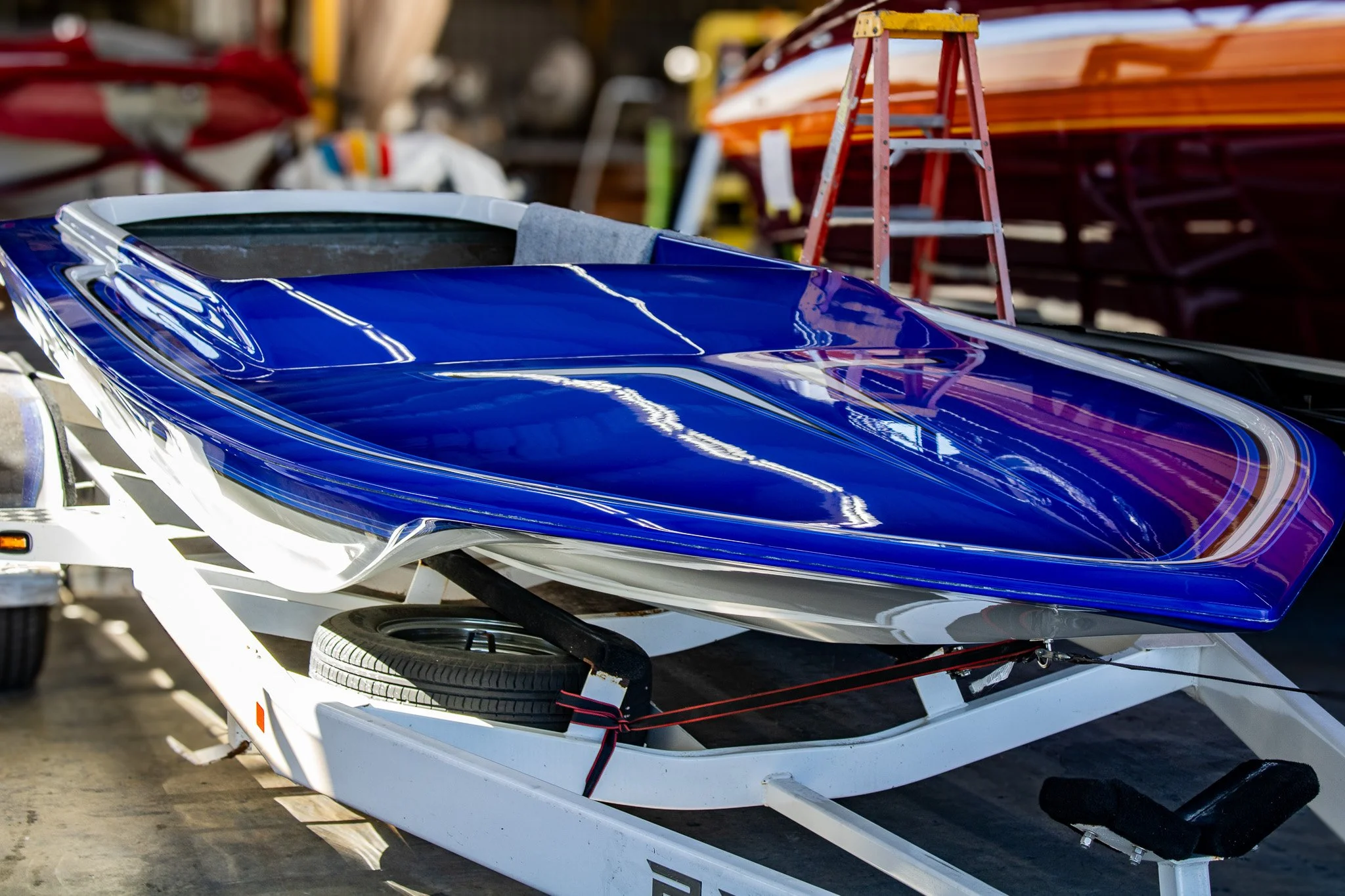 A blue and white speedboat on a trailer in a workshop or storage area with other boats and equipment in the background.