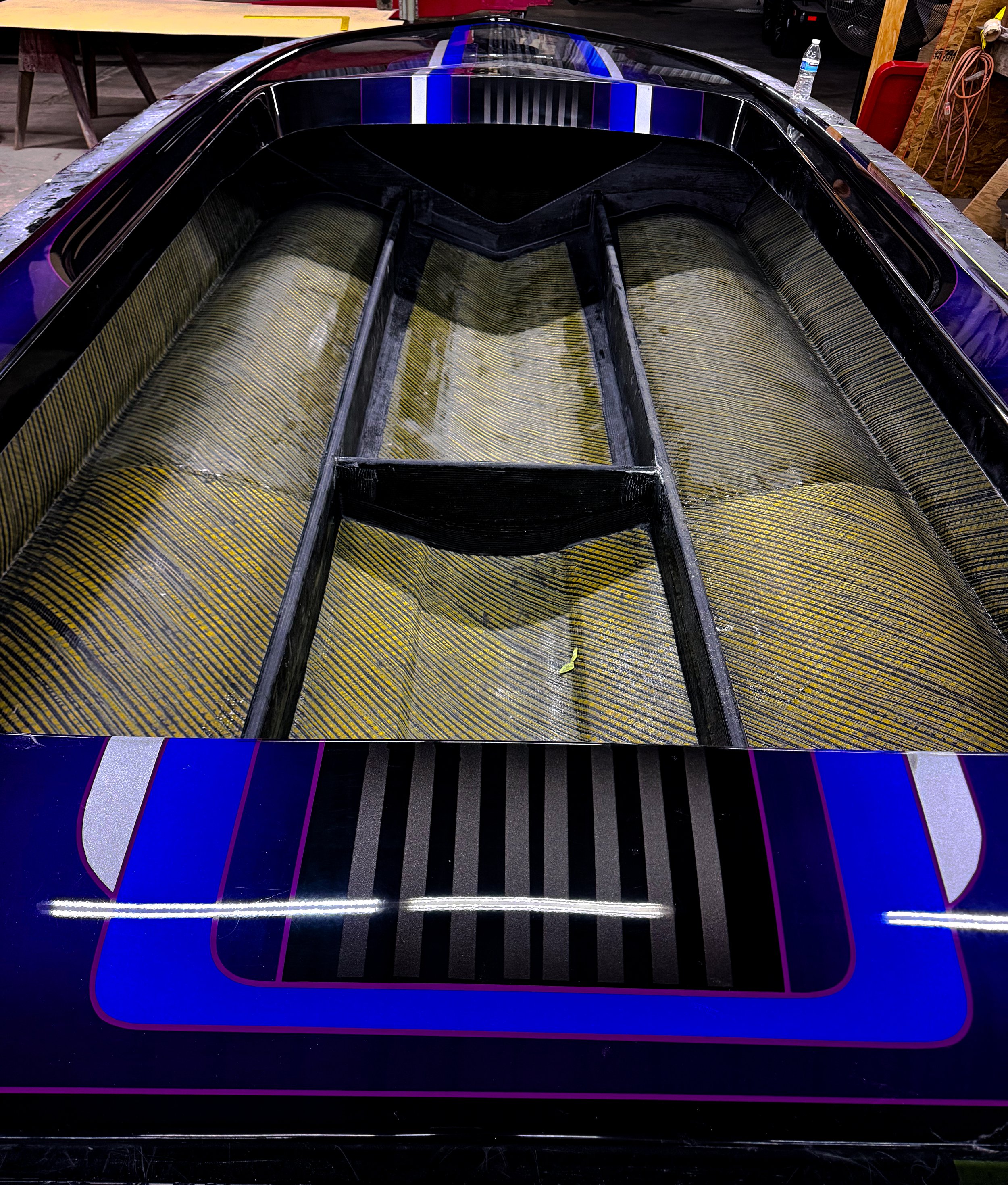 Close-up of a boat hull with black, purple, and blue accents, situated in a workshop or garage.