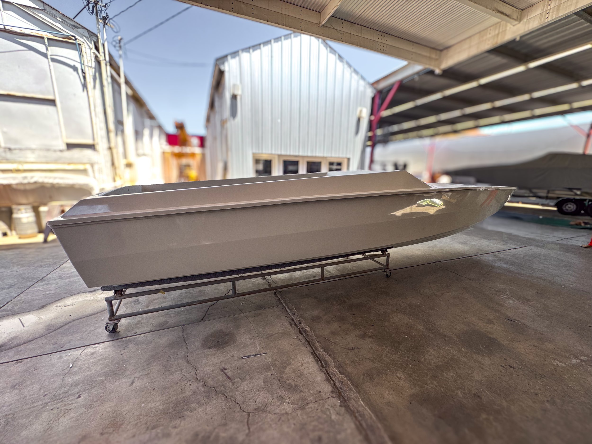 A boat propped up on a wheeled stand inside a garage with storage shelves and a boat behind it.