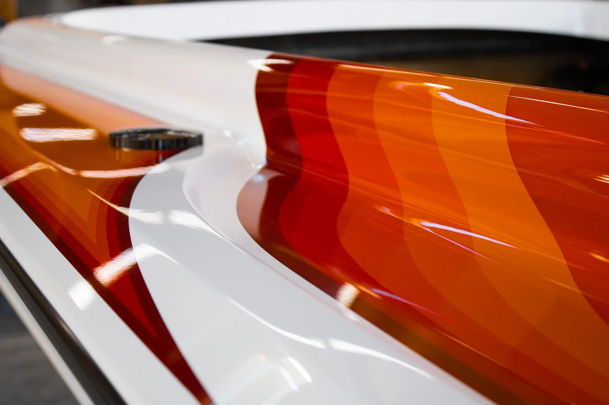 Close-up of a sleek, shiny surface with a color pattern of white, orange, and red, possibly part of a vehicle or an object with a metallic finish.