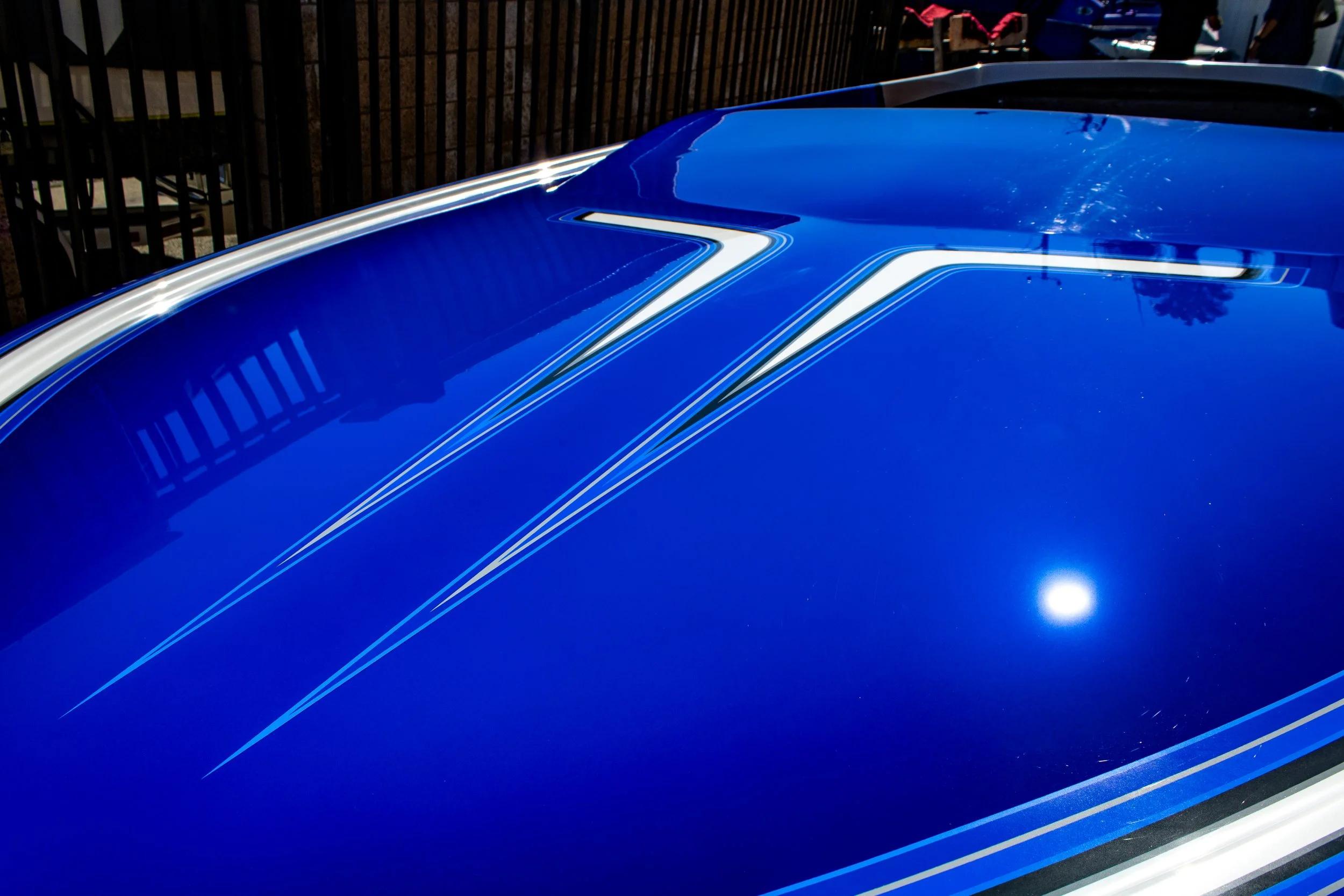 Close-up of a blue boat hull with white racing stripes, reflecting sunlight and surroundings.