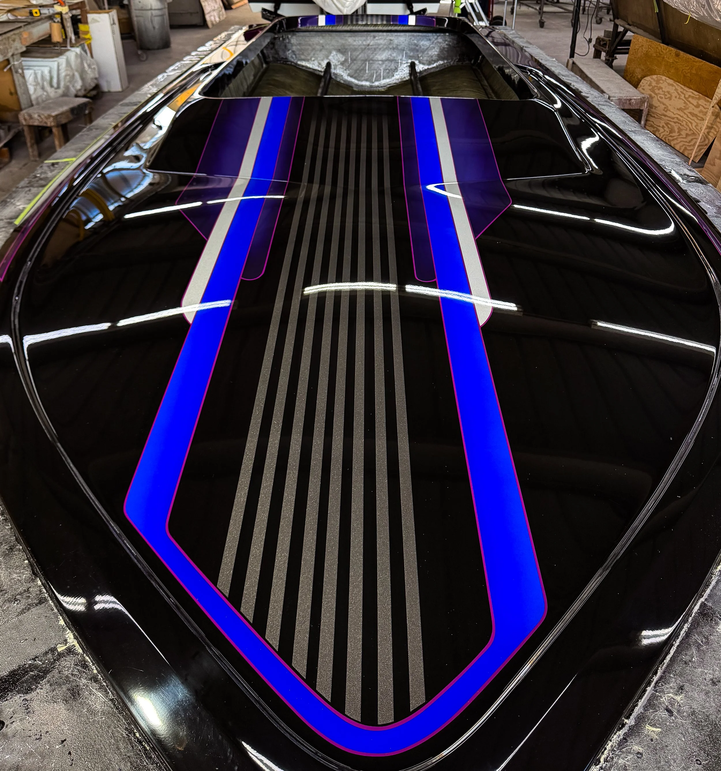 Close-up of a black boat hull with colorful racing stripes in a garage or workshop.