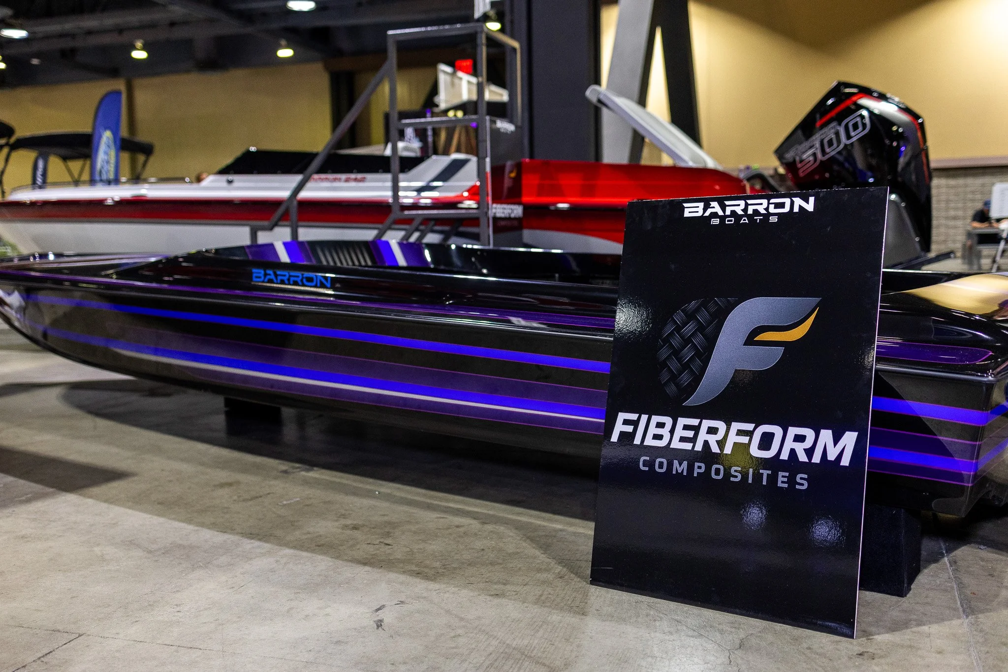 A sleek black and purple speedboat on display at an indoor event, with a sign that reads "FIBERFORM COMPOSITES" in front of it.