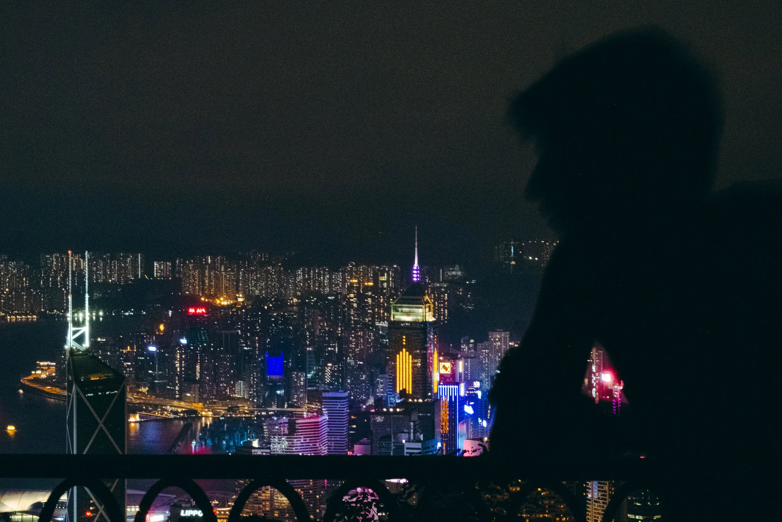 Silhouette de una persona mirando a la ciudad iluminada de noche desde una terraza