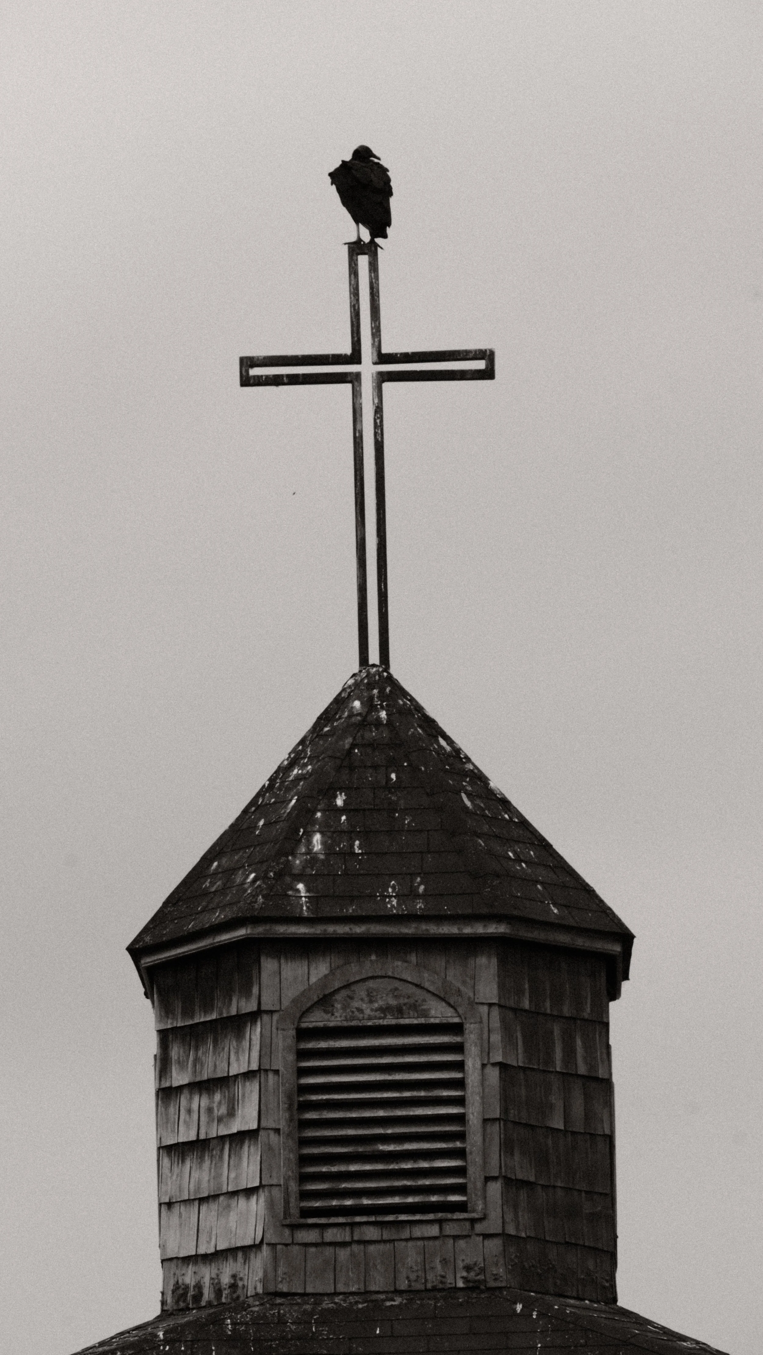 Campanario de madera con campana y una cruz en la parte superior, un águila posada sobre la cruz.