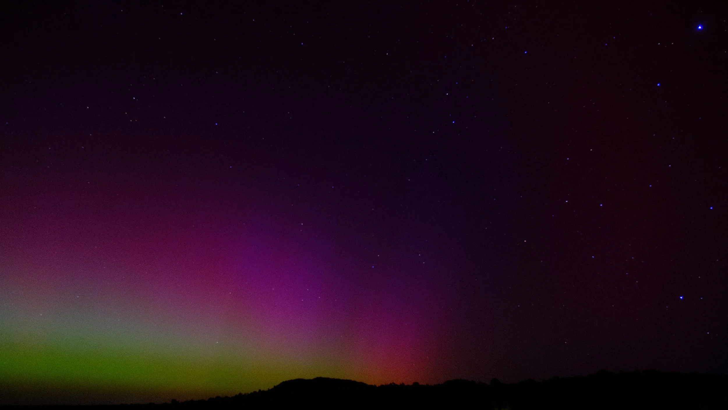 Aurora boreal en el cielo nocturno con estrellas y un paisaje de montañas en la parte inferior