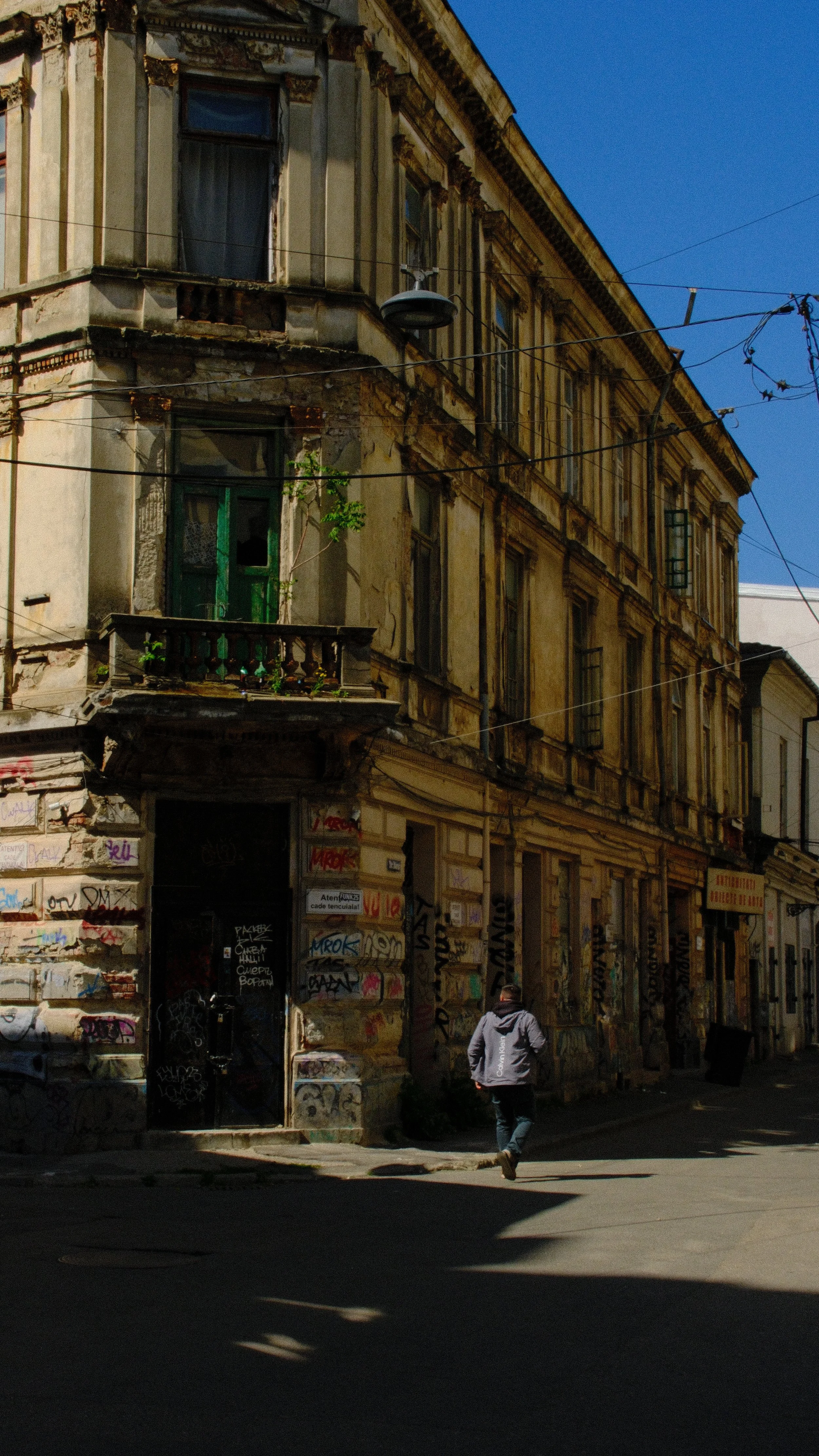 Edificio antiguo con paredes desgastadas y graffiti en la calle, persona caminando.