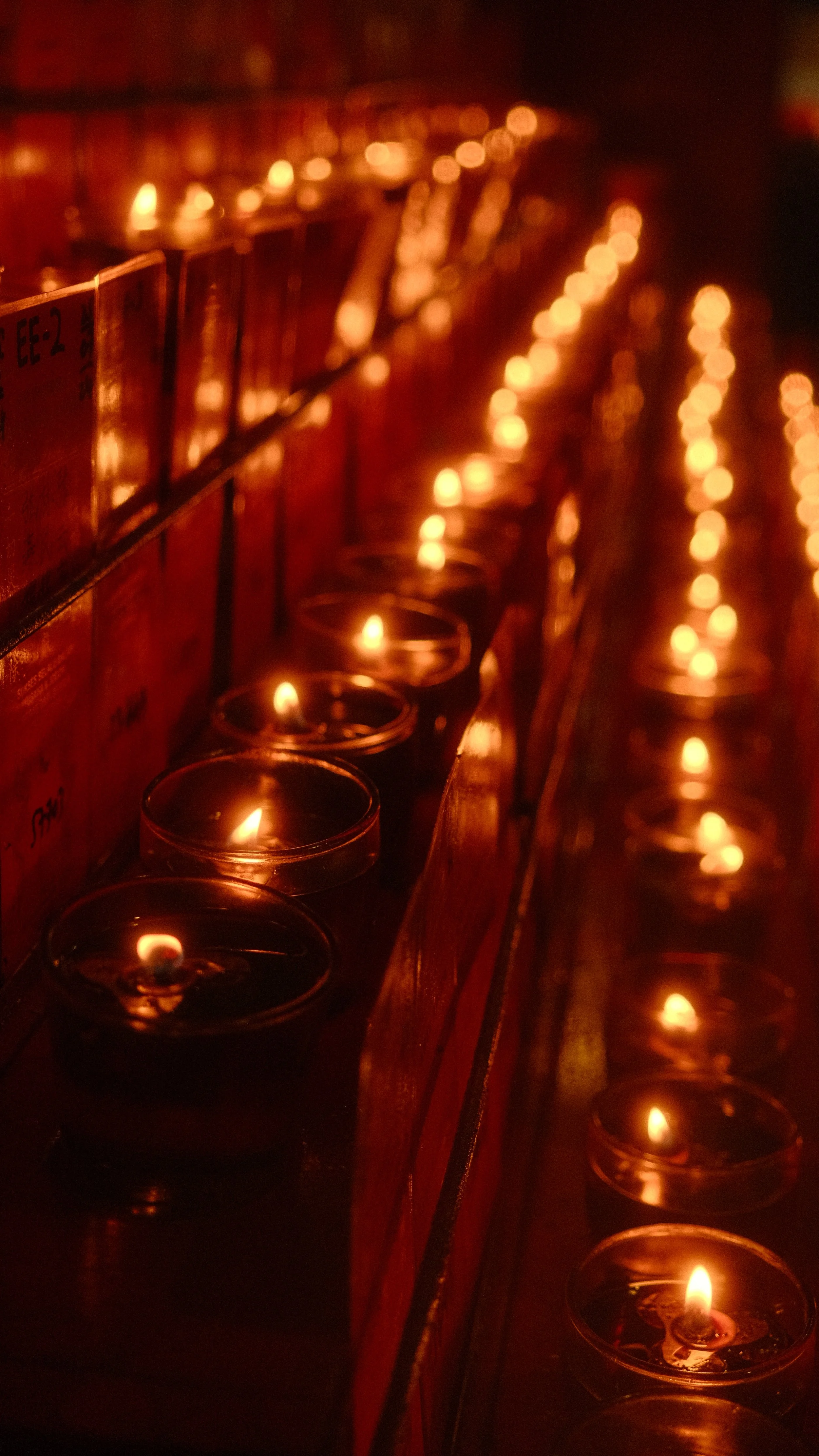 Vela encendida en un candelabro, con muchas velas similares alineadas en la misma fila, creando un ambiente cálido y solemne.