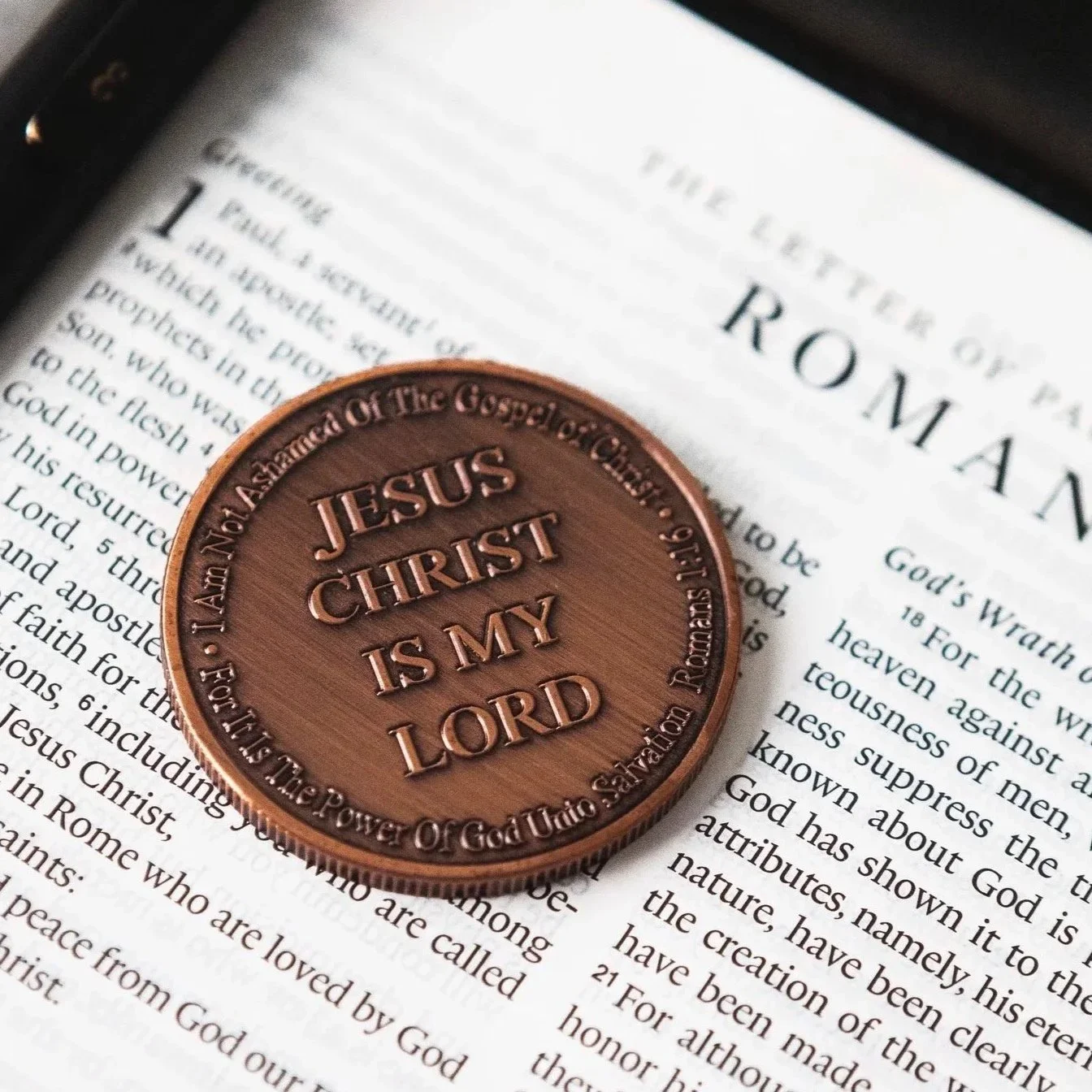 Close-up of a religious medal with the inscription 'Jesus Christ Is My Lord' resting on an open Bible with readable text about Jesus and Christian beliefs.