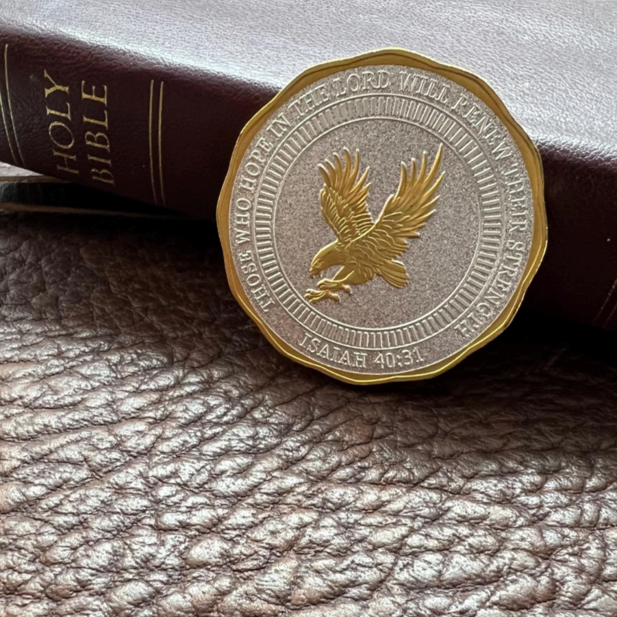 Close-up of a silver and gold coin with an eagle, resting against a leather-bound Bible on a textured brown surface.