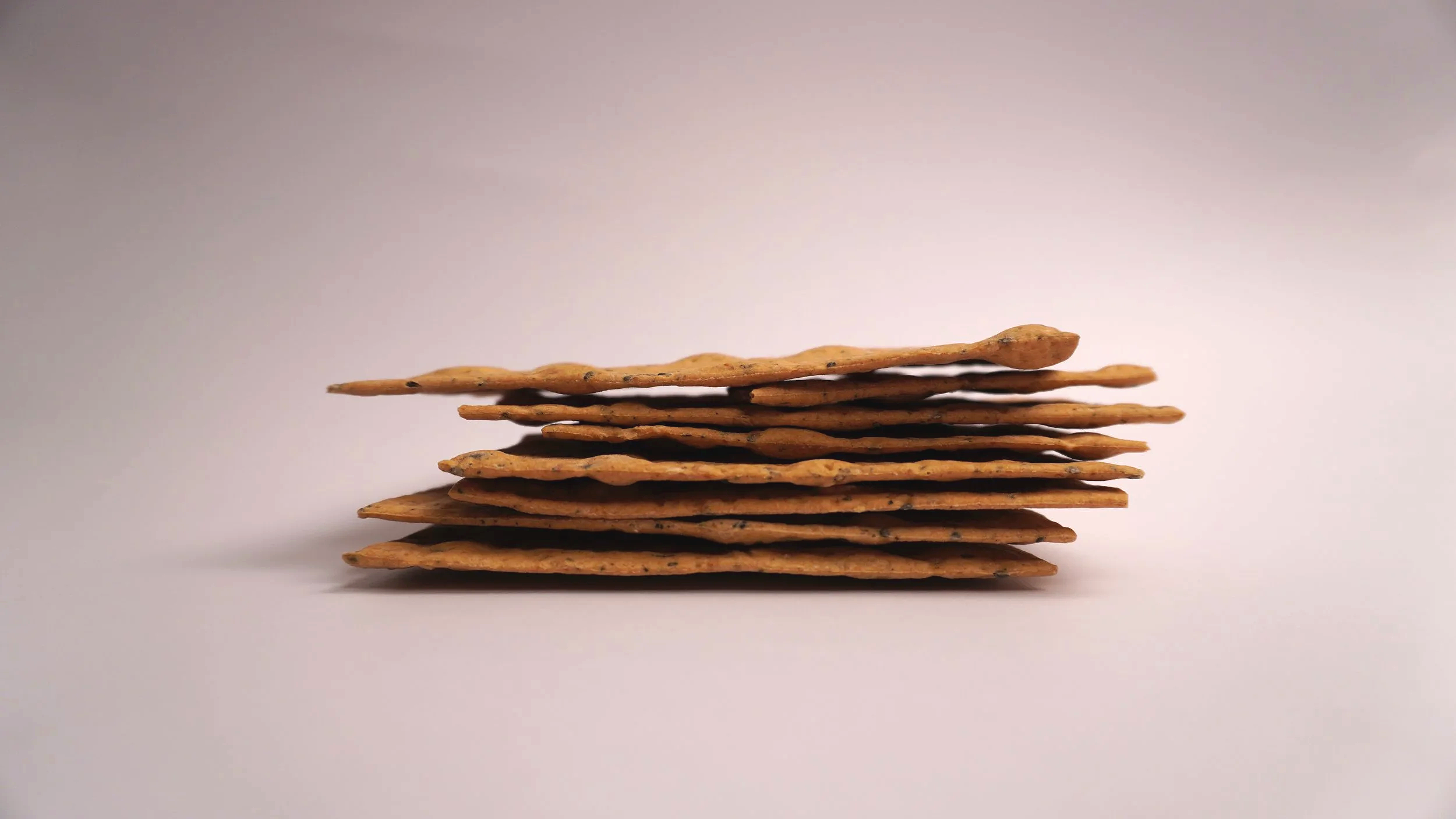 A stack of several rectangular, thin, and crunchy crackers with black specks on a plain white background.