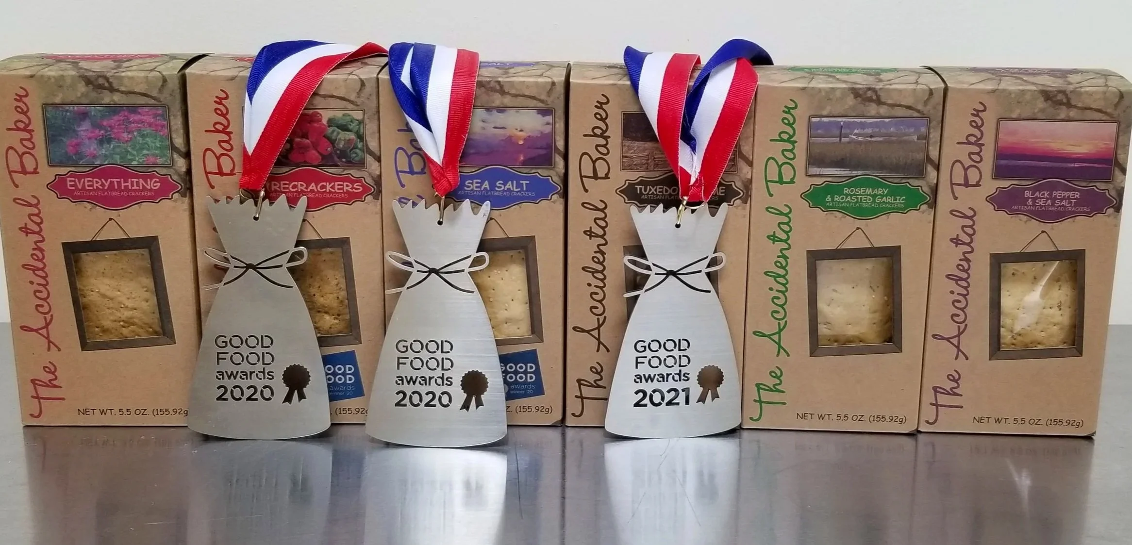 All six artisan flatbread cracker flavors  with  three medals for 'Good Food Awards 2020 and 2021.' Sea Salt, Tuxedo Sesame, Rosemary & Roasted Garlic, Black Pepper & Sea Salt, and Everything.