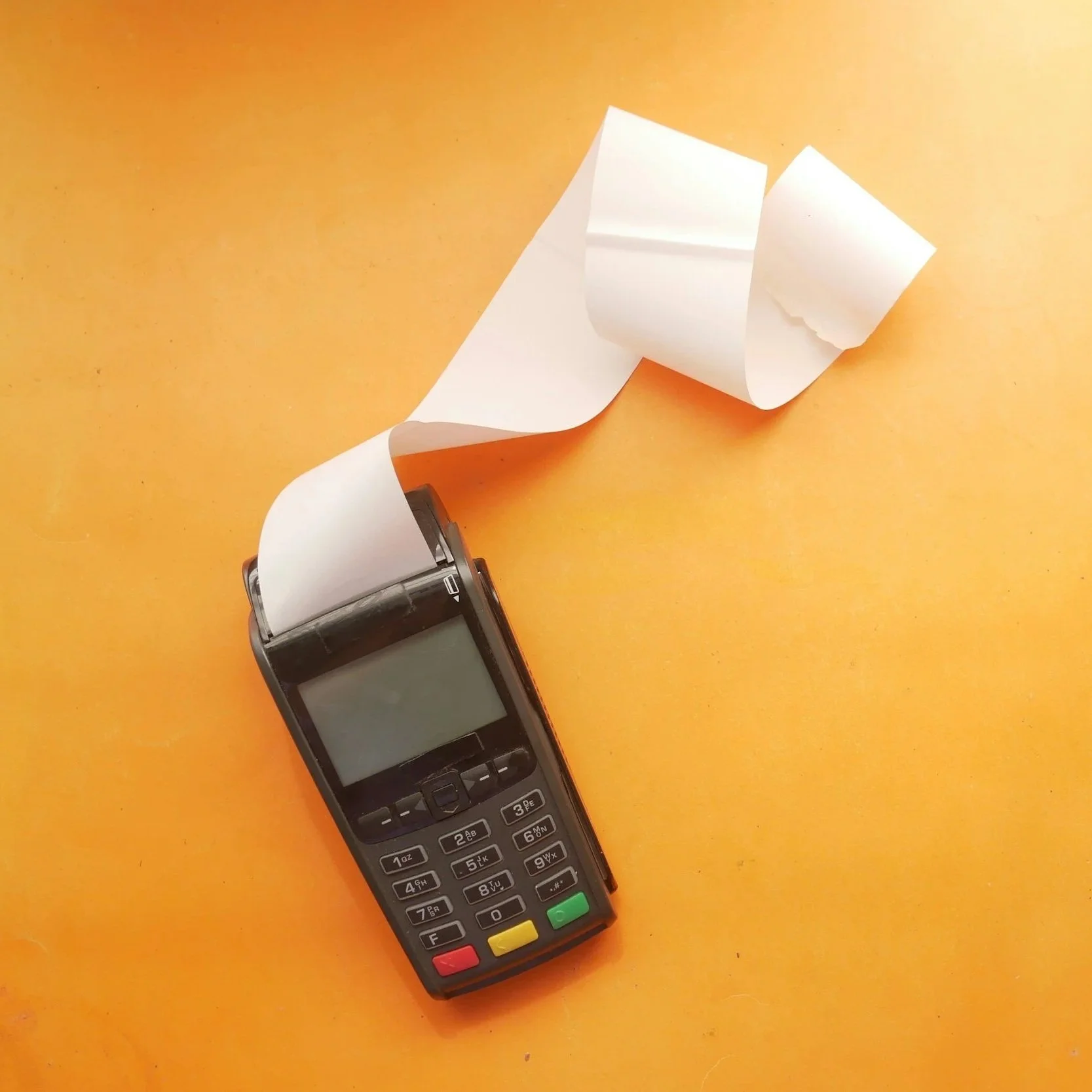 Point of sale terminal with printed receipt on orange background.