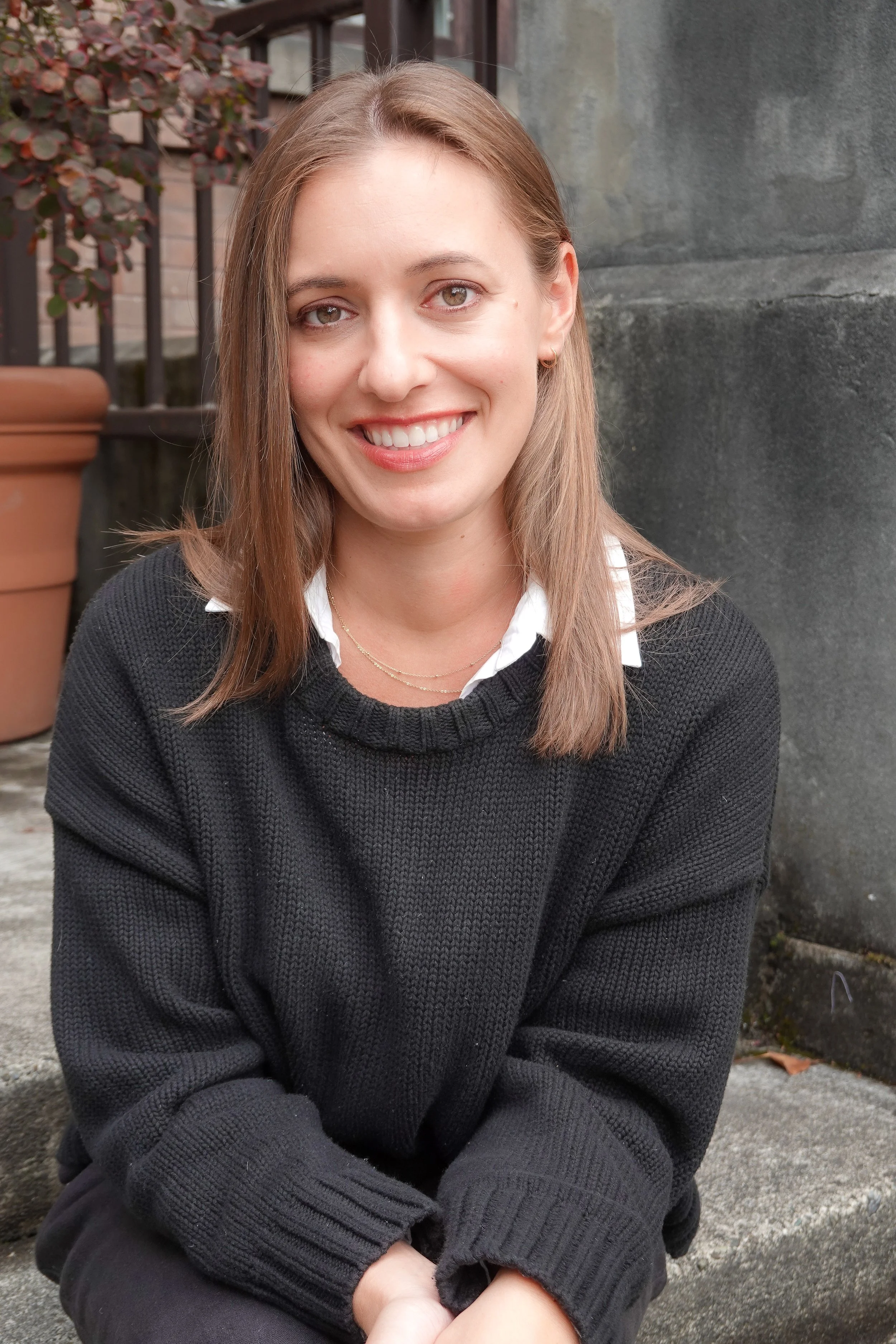 Sarah Stewart, Seattle therapist, smiling outdoors near a concrete wall and potted plant