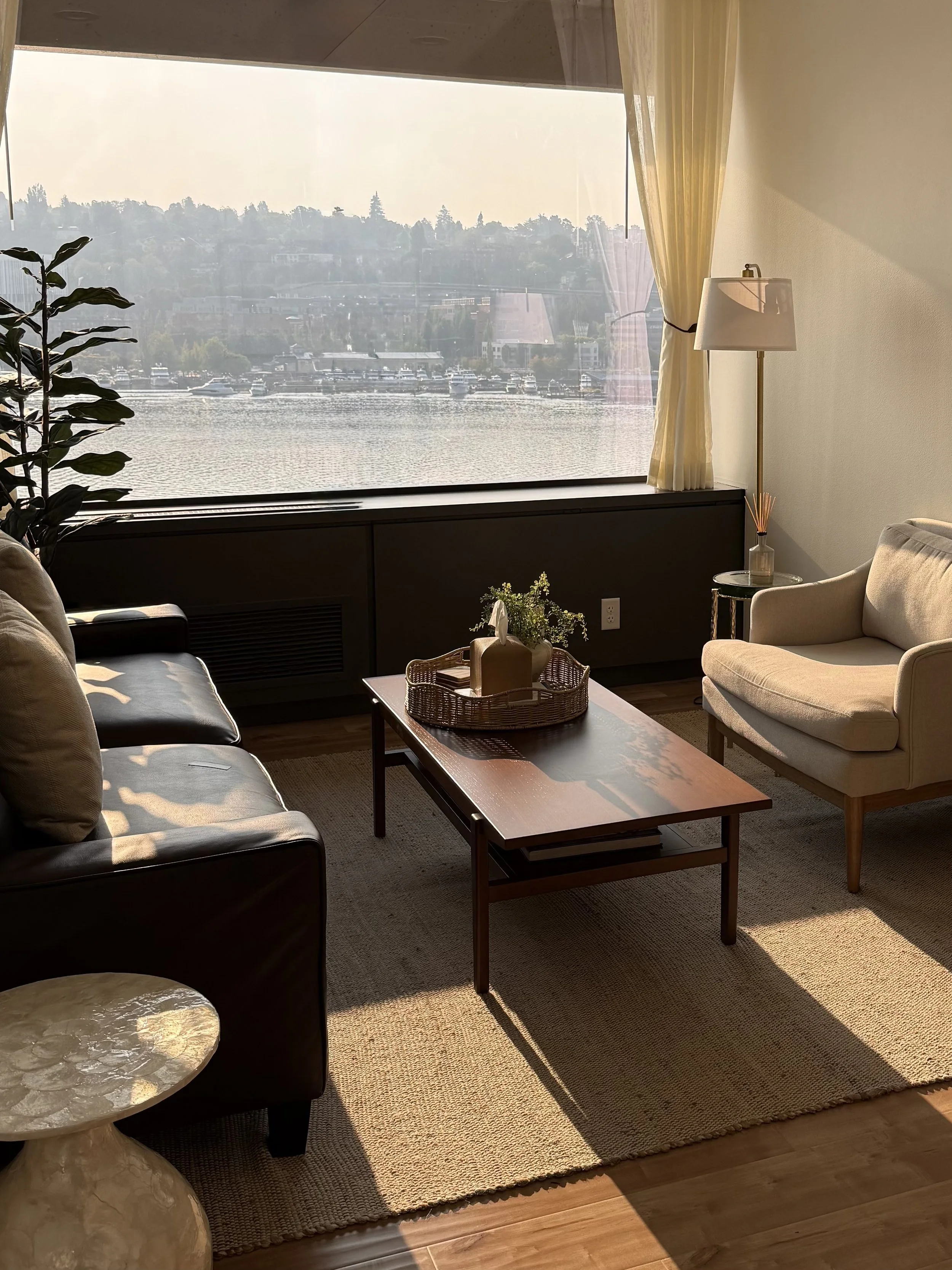 A therapy office in Seattle with a brown leather sofa and armchair around a wood coffee table, looking out over the water.