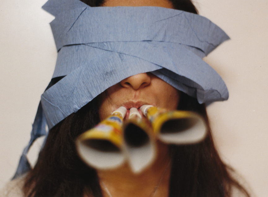 Person wearing a paper hat and with party blowers in their mouth.