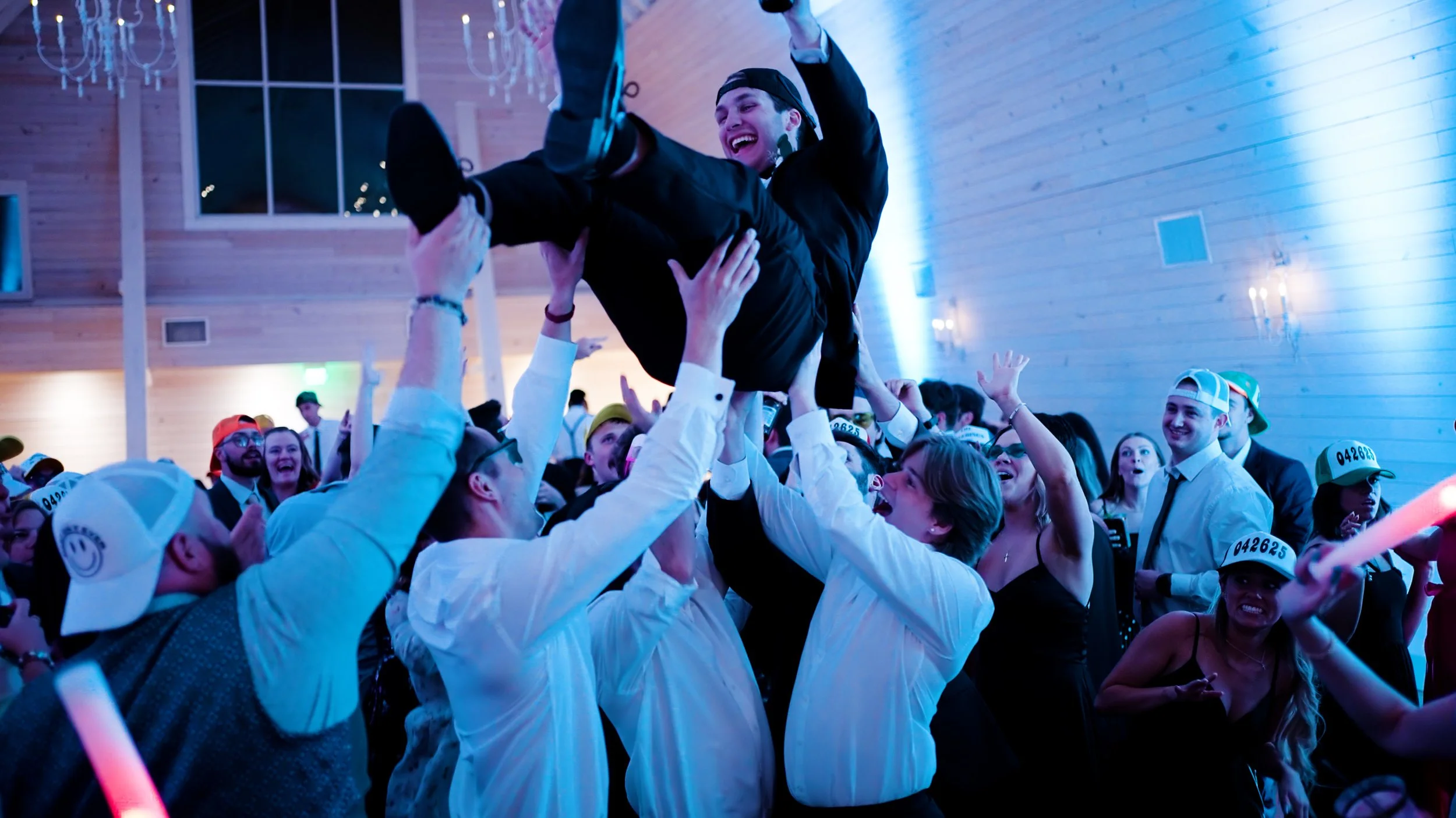 People celebrating at a wedding, lifting a young man into the air.