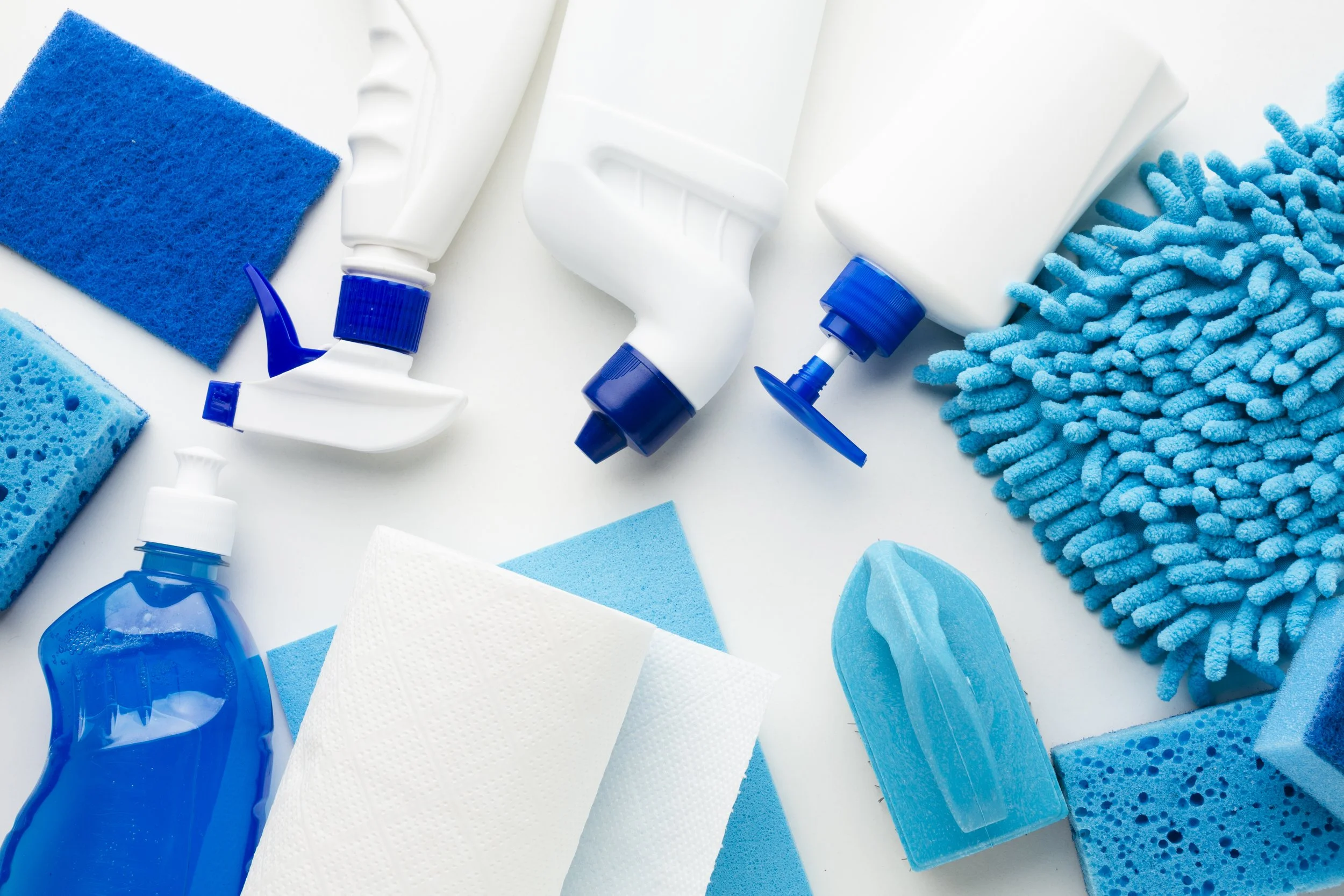 Various cleaning supplies including spray bottles, sponges, a scrub brush, cloths, and a mop in blue and white colors, arranged on a white background.